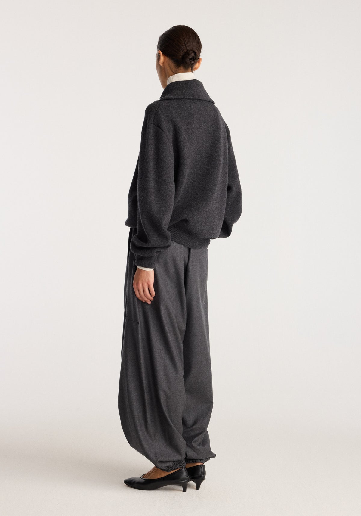 Reversible zipped turtleneck | charcoal shown from the back on a model with relaxed dark trousers and black heels in a neutral studio setting