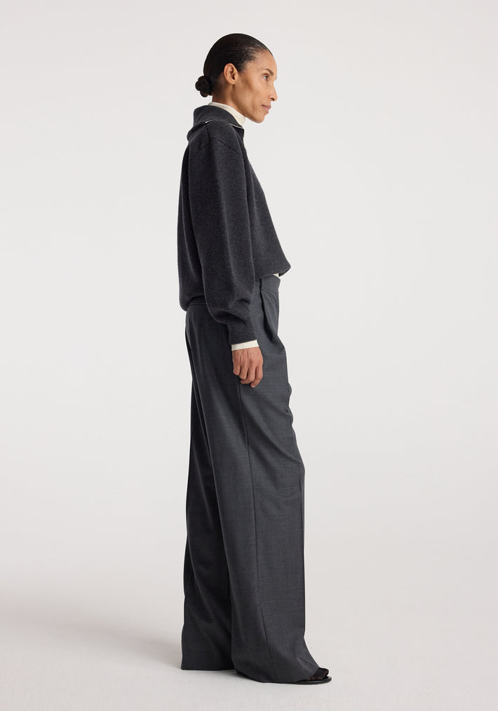 Woman wearing a charcoal Two-way zipped turtleneck | charcoal with long sleeves and loose fit, paired with high-waisted dark gray wide-leg trousers against a plain background.