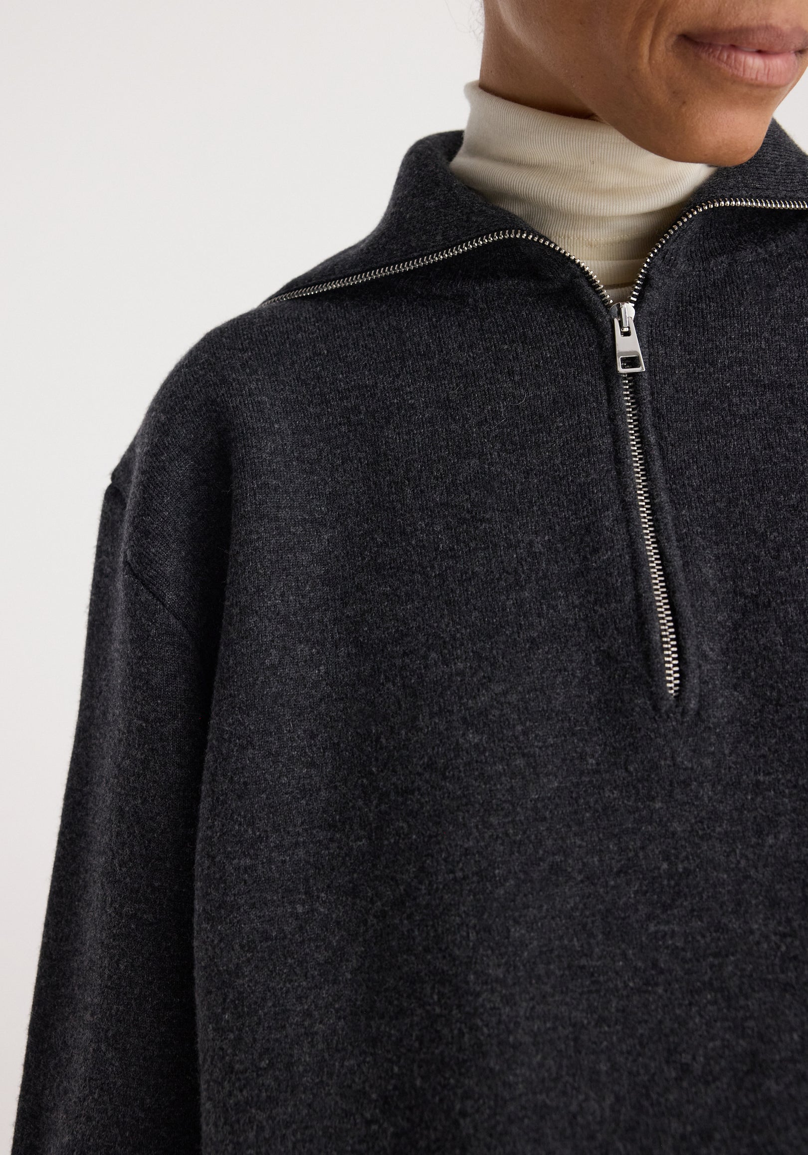 Close-up of a person wearing a charcoal Two-way zipped turtleneck | charcoal layering over a light beige turtleneck, featuring a half-zip design and soft textured fabric.