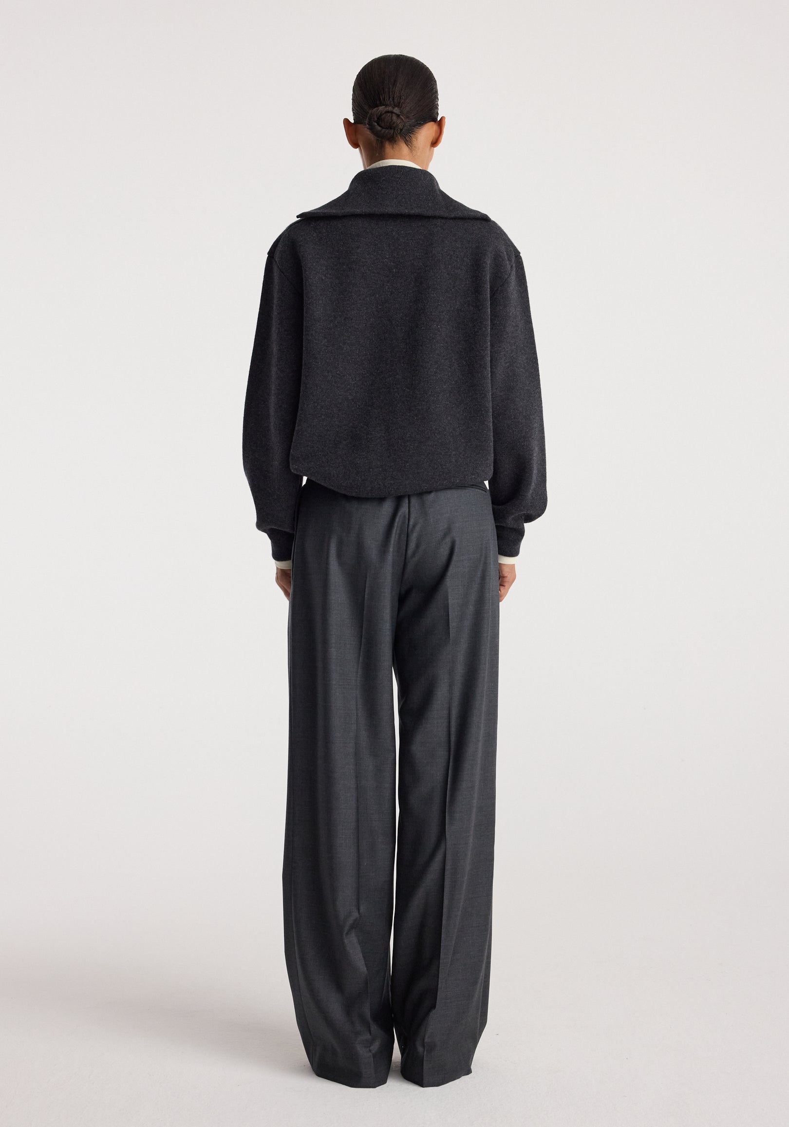 Back view of a person wearing a charcoal Two-way zipped turtleneck with long sleeves paired with loose dark gray trousers against a plain white background.