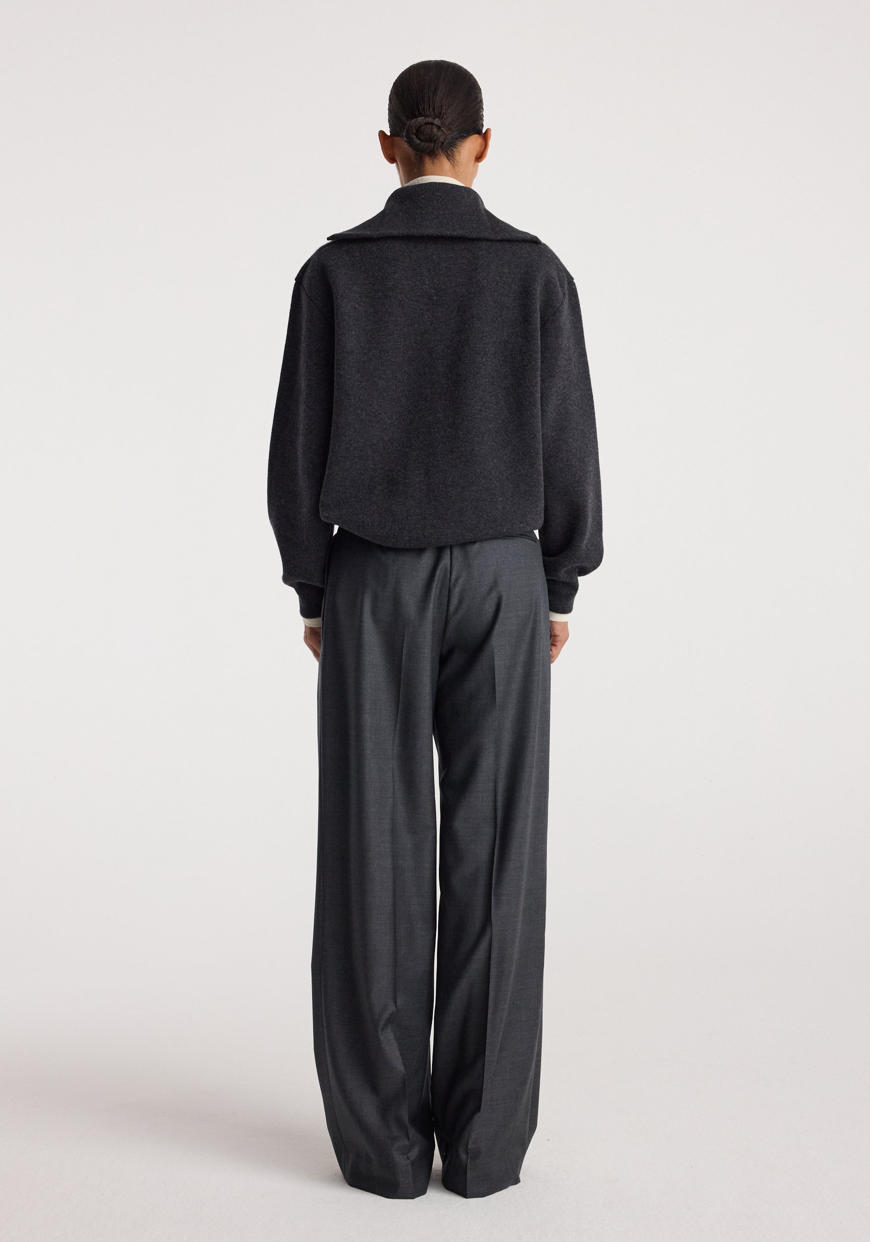 Back view of a person wearing a charcoal Two-way zipped turtleneck with long sleeves paired with loose dark gray trousers against a plain white background.