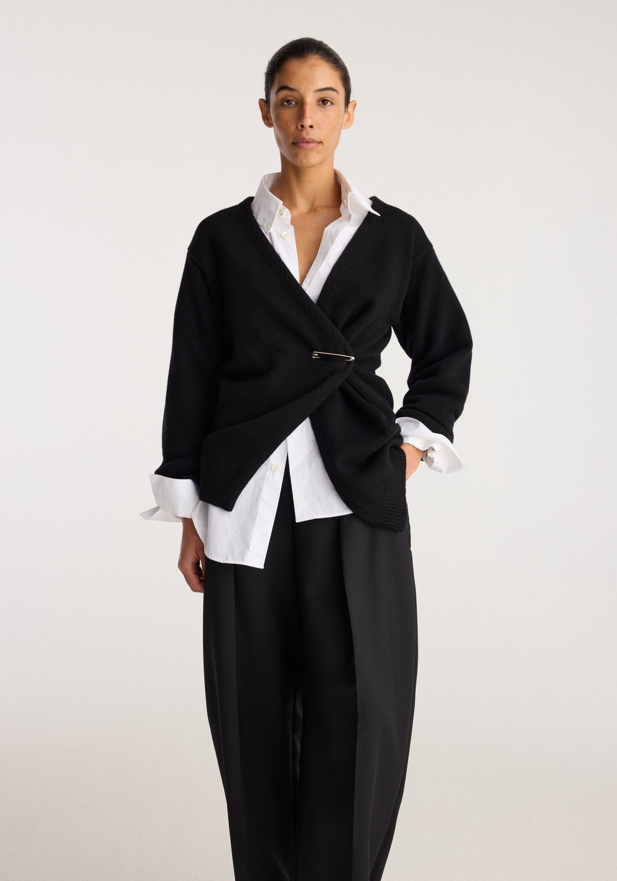 Off-shoulder wrap cardigan | black styled over a white shirt with a wrap front and clasp detail on a model