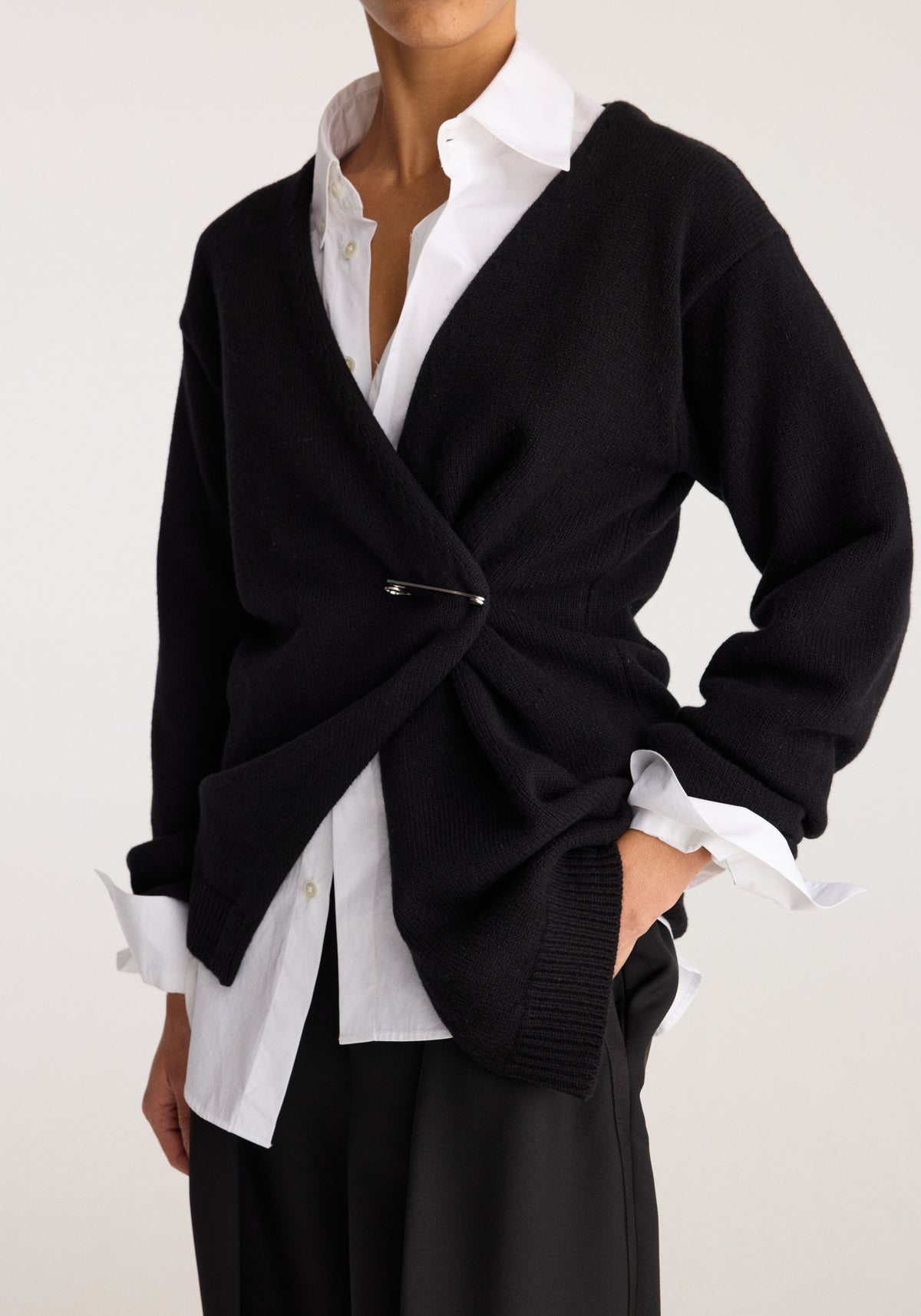 Off-shoulder wrap cardigan | black worn over a white collared shirt with long sleeves and a cinched wrap front in a studio fashion photo