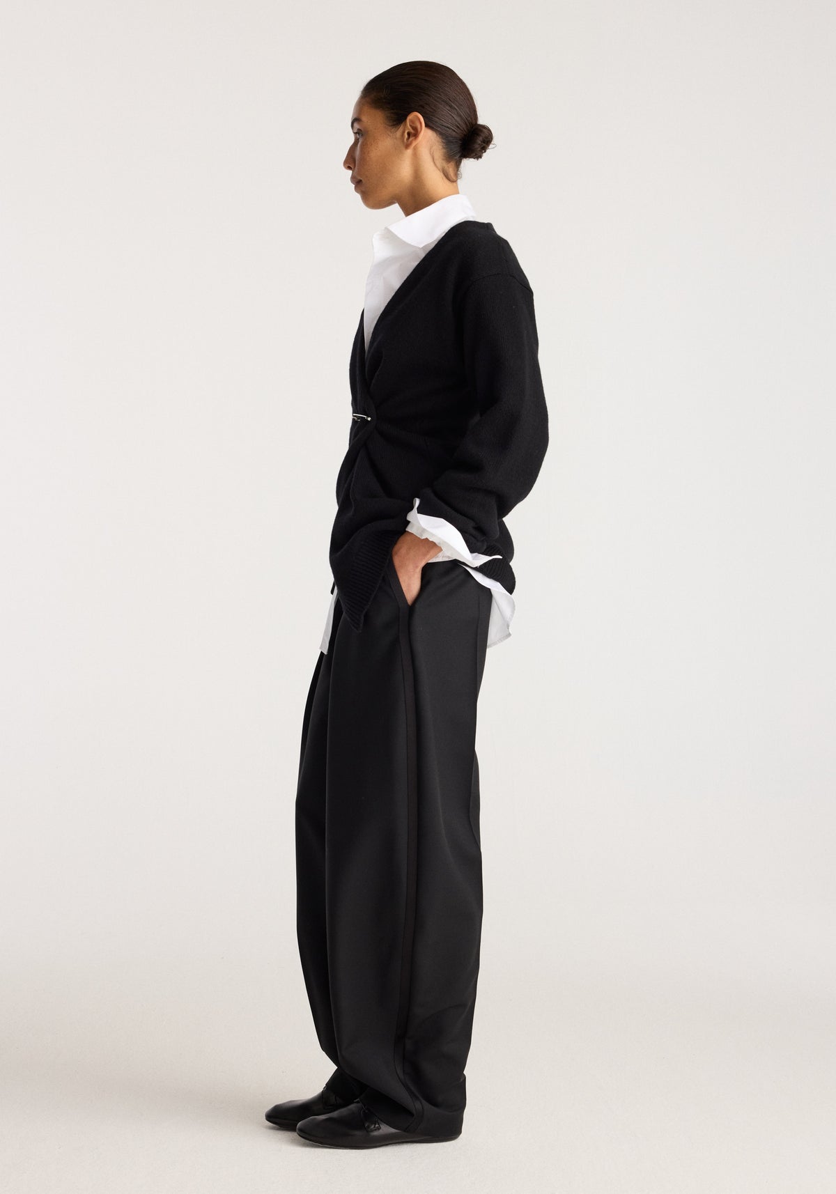Off-shoulder wrap cardigan | black shown in side profile on a model over a white collared shirt with black trousers.