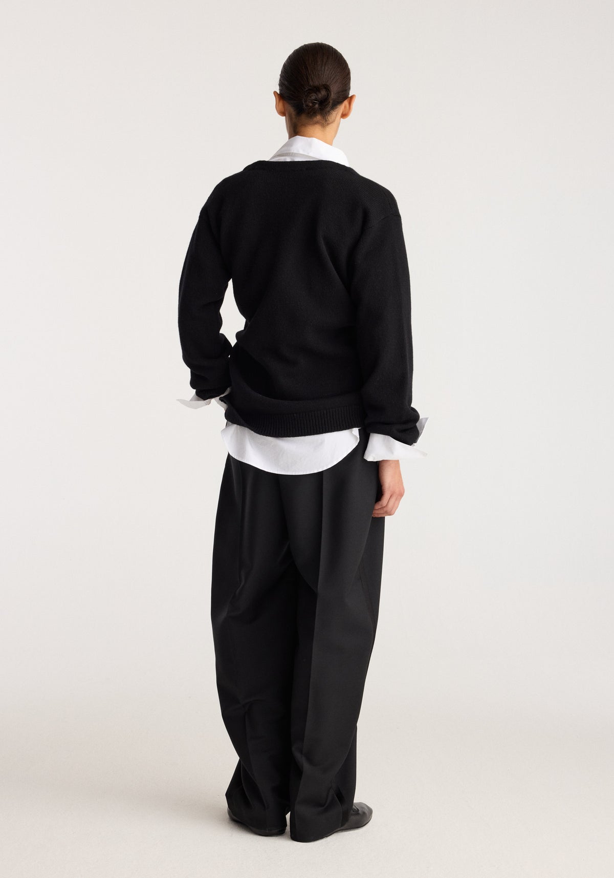 Off-shoulder wrap cardigan | black shown from the back on a model layered over a white shirt with black trousers in a studio setting