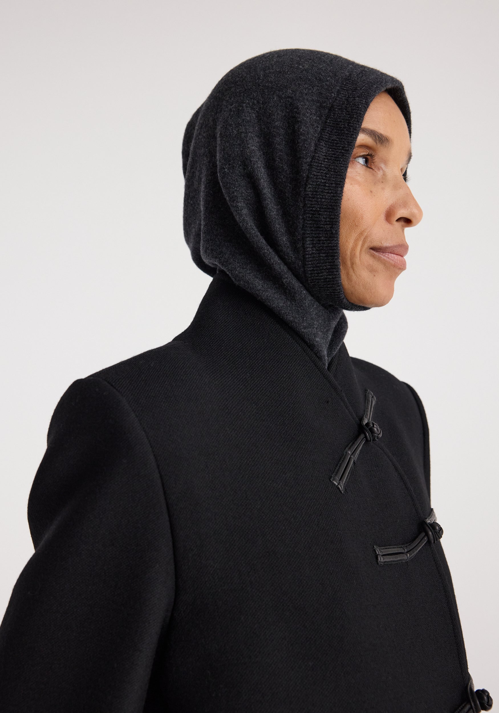 Profile of a person wearing a Balaclava | anthracite melange in dark grey fabric, paired with a black coat featuring toggle closures.