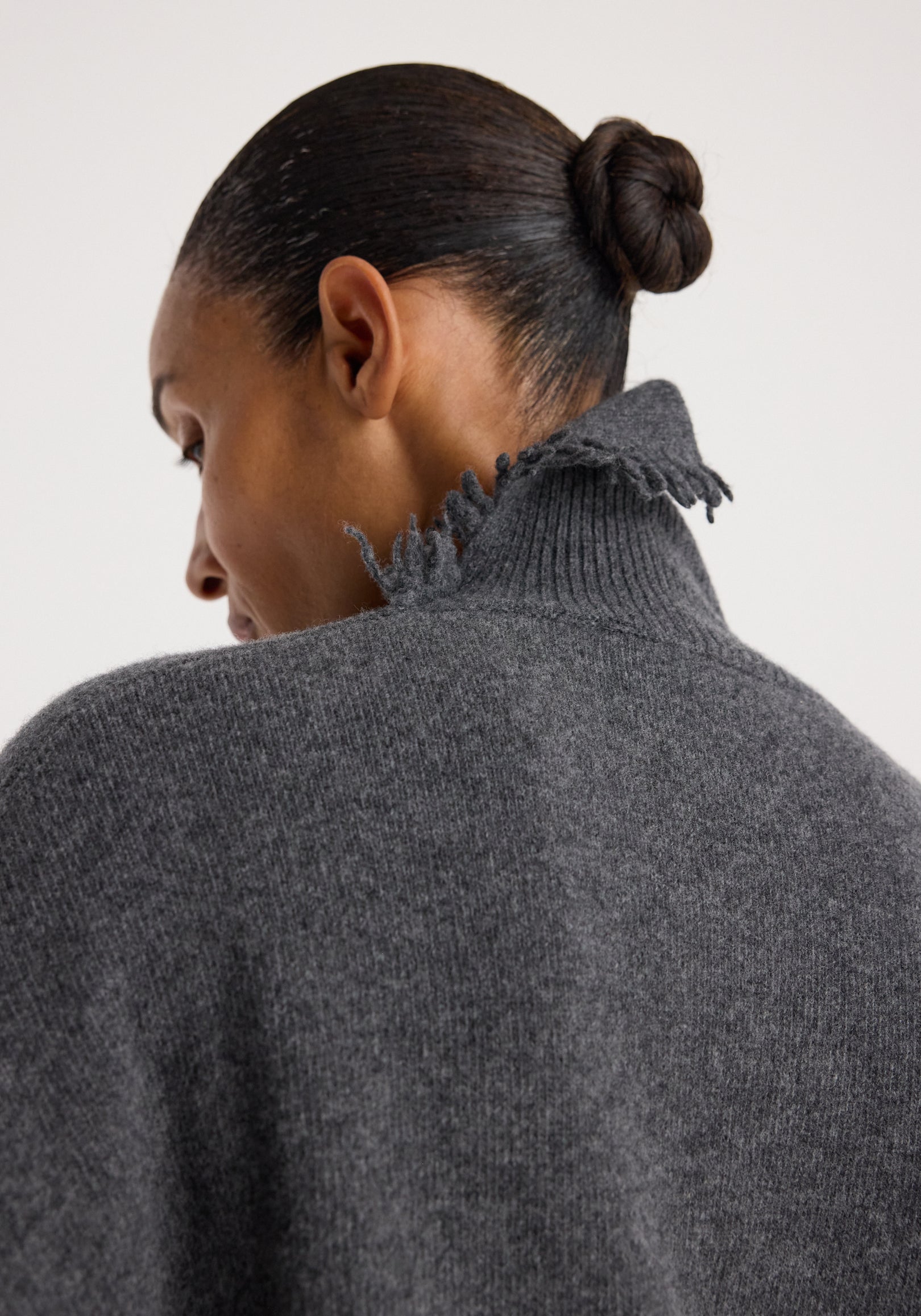Close-up back view of a person wearing a Turtleneck with raw details | dark grey melange, showcasing the textured fabric and frayed high collar.