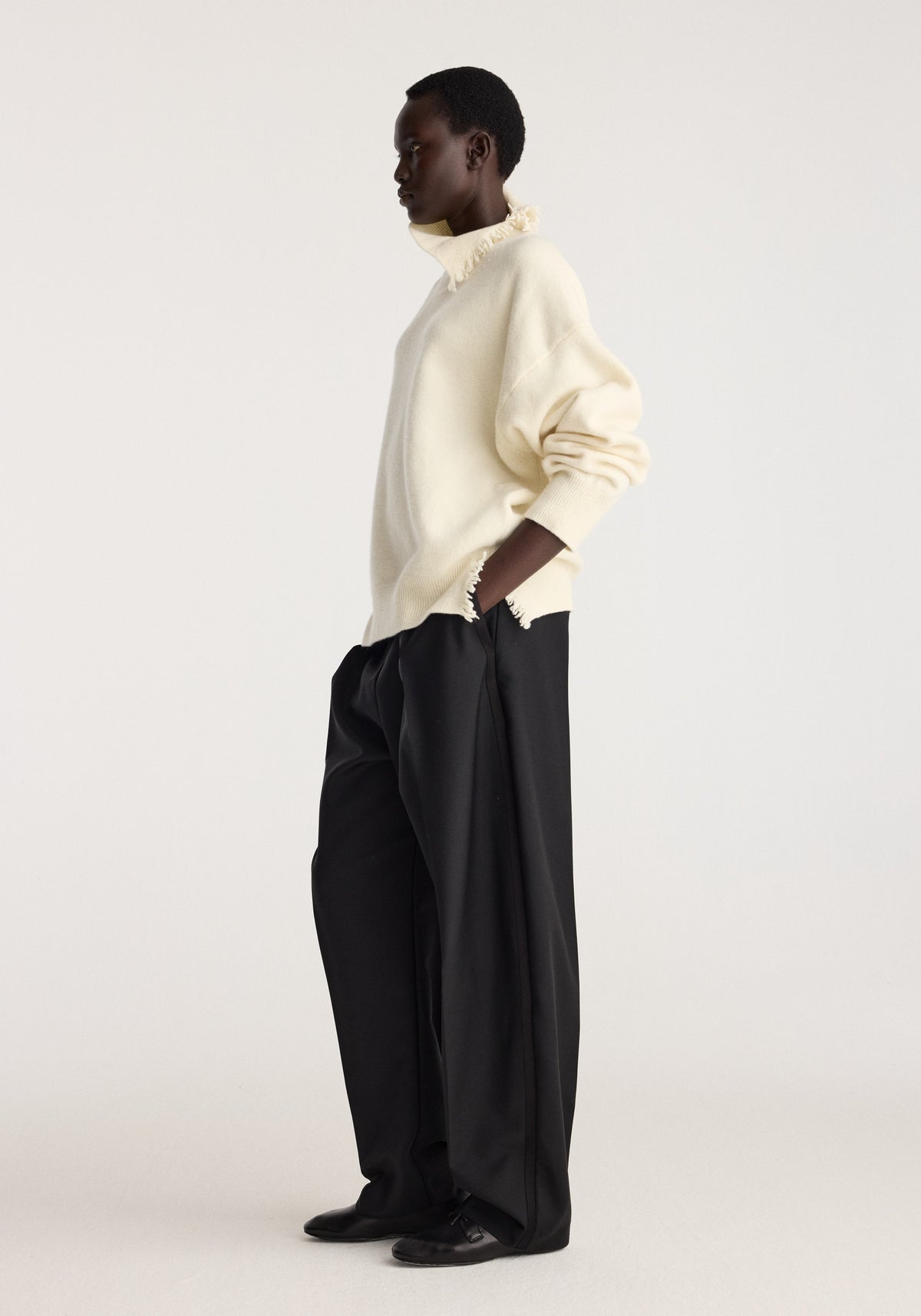 Turtleneck with raw details | off white worn by a model in profile with black wide leg trousers and dark shoes against a light studio background