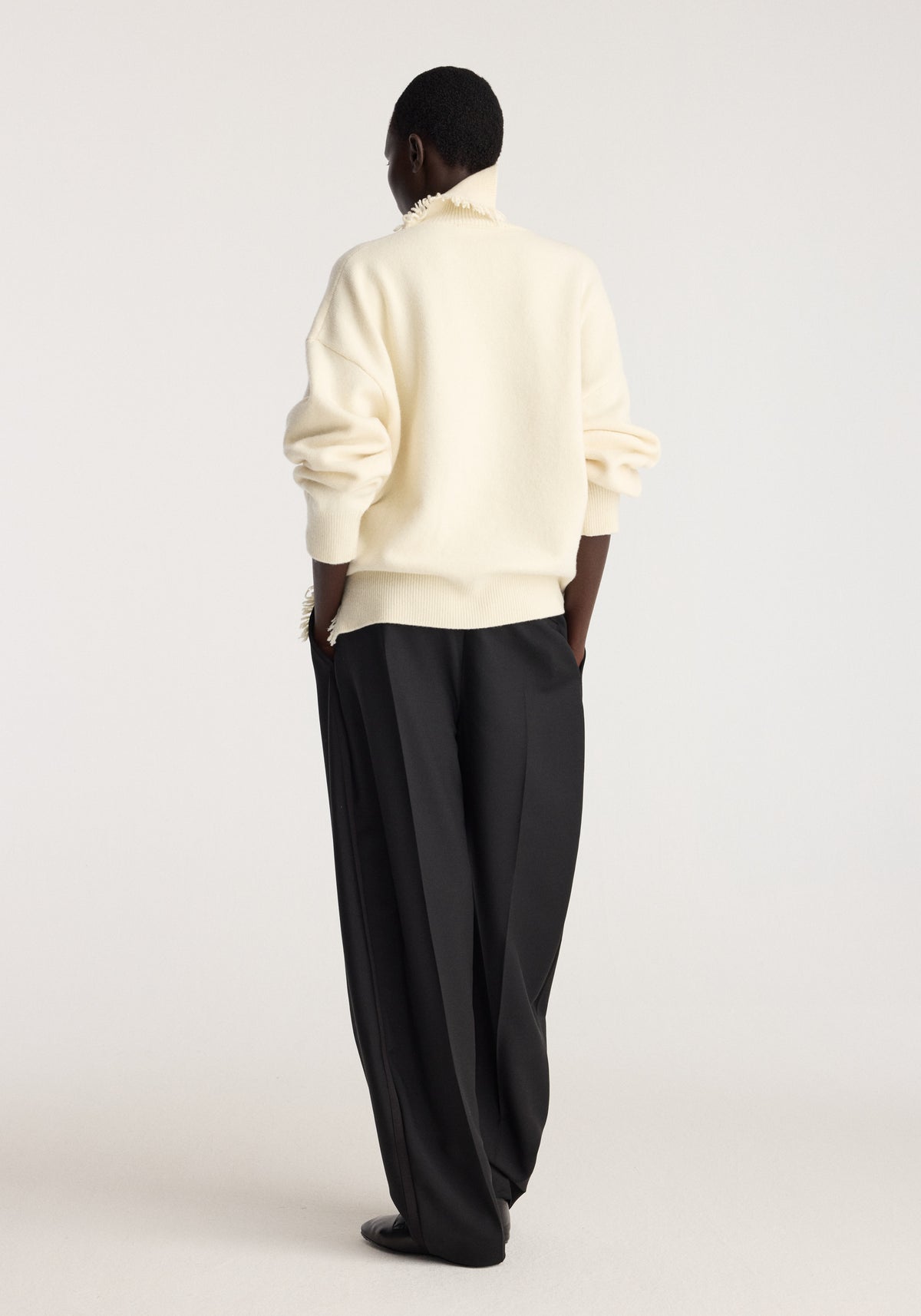 Turtleneck with raw details | off white shown from the back on a model with rolled sleeves and relaxed black trousers against a neutral studio backdrop