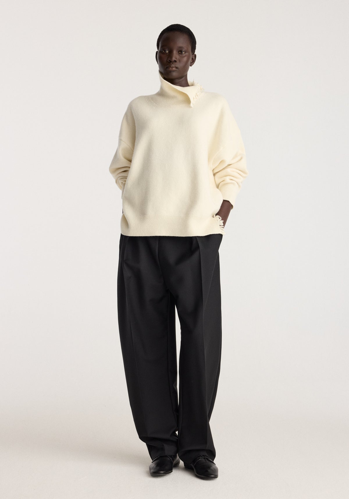 Turtleneck with raw details | off white worn by a model with black trousers in a studio featuring a high neck and relaxed sleeves