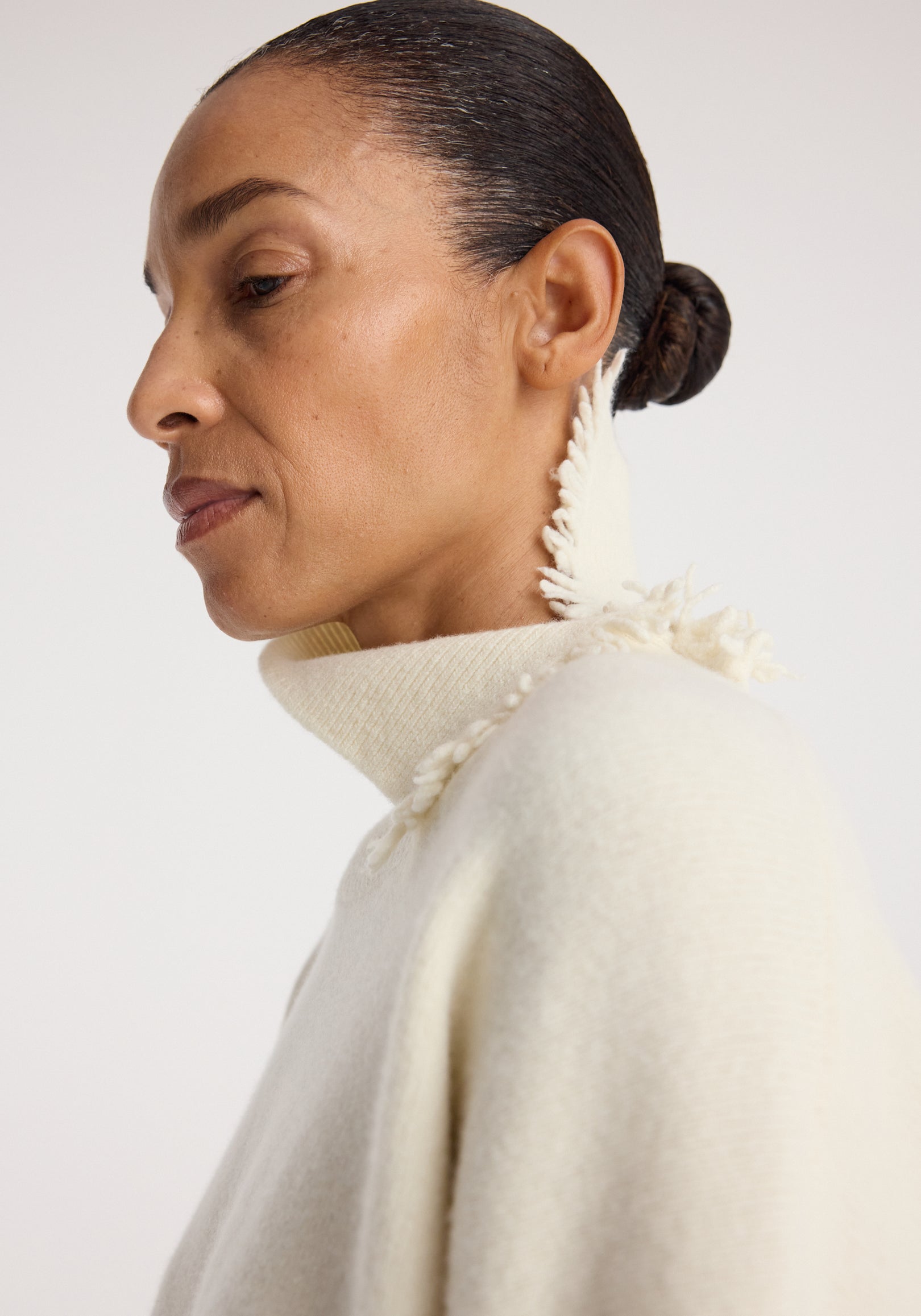 Close-up profile of a woman wearing a soft off-white Turtleneck with raw details | off white featuring a high neckline with frayed edges and textured fabric accents.