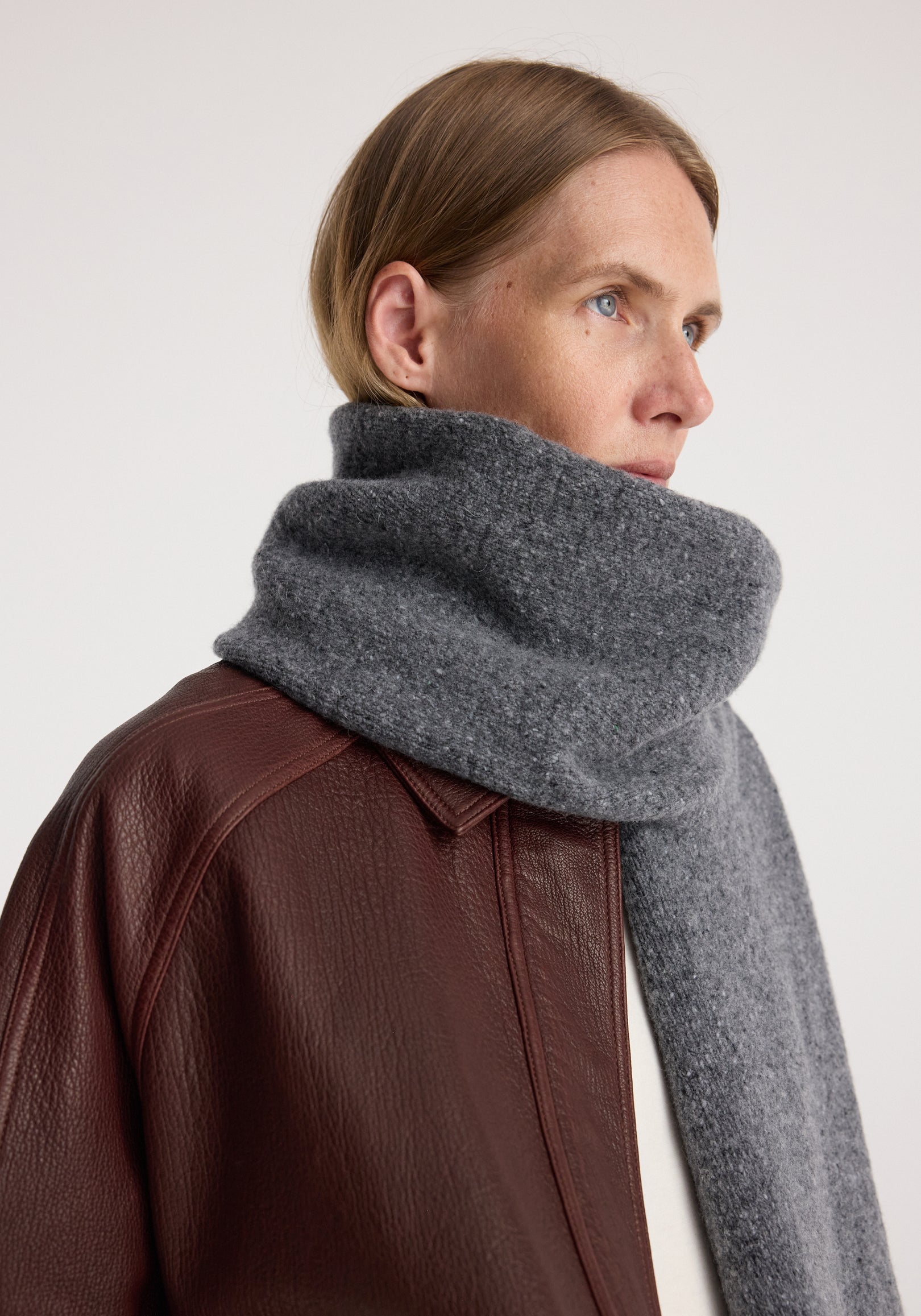 Woman wearing a cozy Knitted mouliné scarf | anthracite melange wrapped around her neck paired with a brown textured leather jacket.