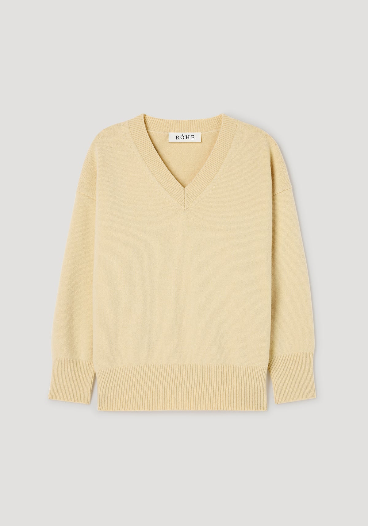 Classic v-neck jumper | butter in a soft light yellow shade with long sleeves, ribbed cuffs, hem, and neckline, displayed on a plain light gray background.