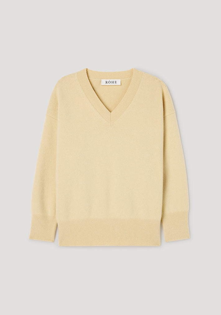 Classic v-neck jumper | butter in a soft light yellow shade with long sleeves, ribbed cuffs, hem, and neckline, displayed on a plain light gray background.