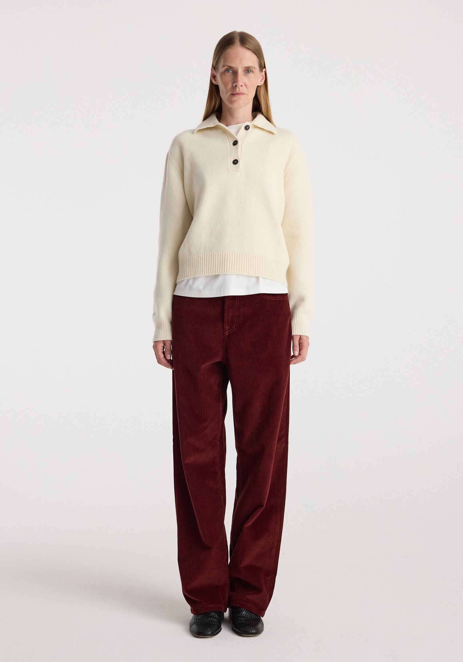Woman wearing Bruun - Signature baggy corduroy trousers | wine paired with a cream long-sleeve sweater and black shoes, standing against a plain white background.