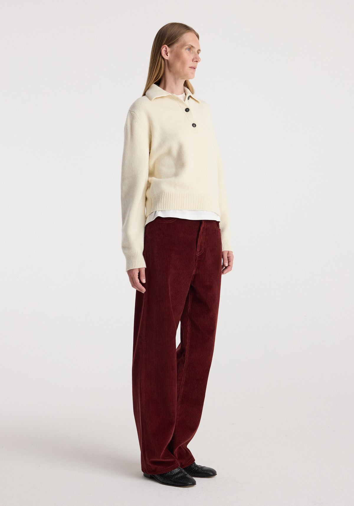 Woman wearing Bruun - Signature baggy corduroy trousers | wine paired with a cream long-sleeve sweater and black shoes, standing against a plain white background.