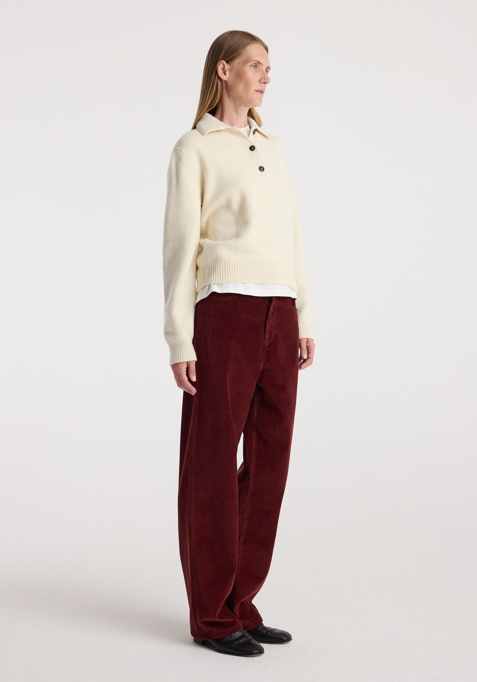 Woman wearing Bruun - Signature baggy corduroy trousers | wine paired with a cream long-sleeve sweater and black shoes, standing against a plain white background.