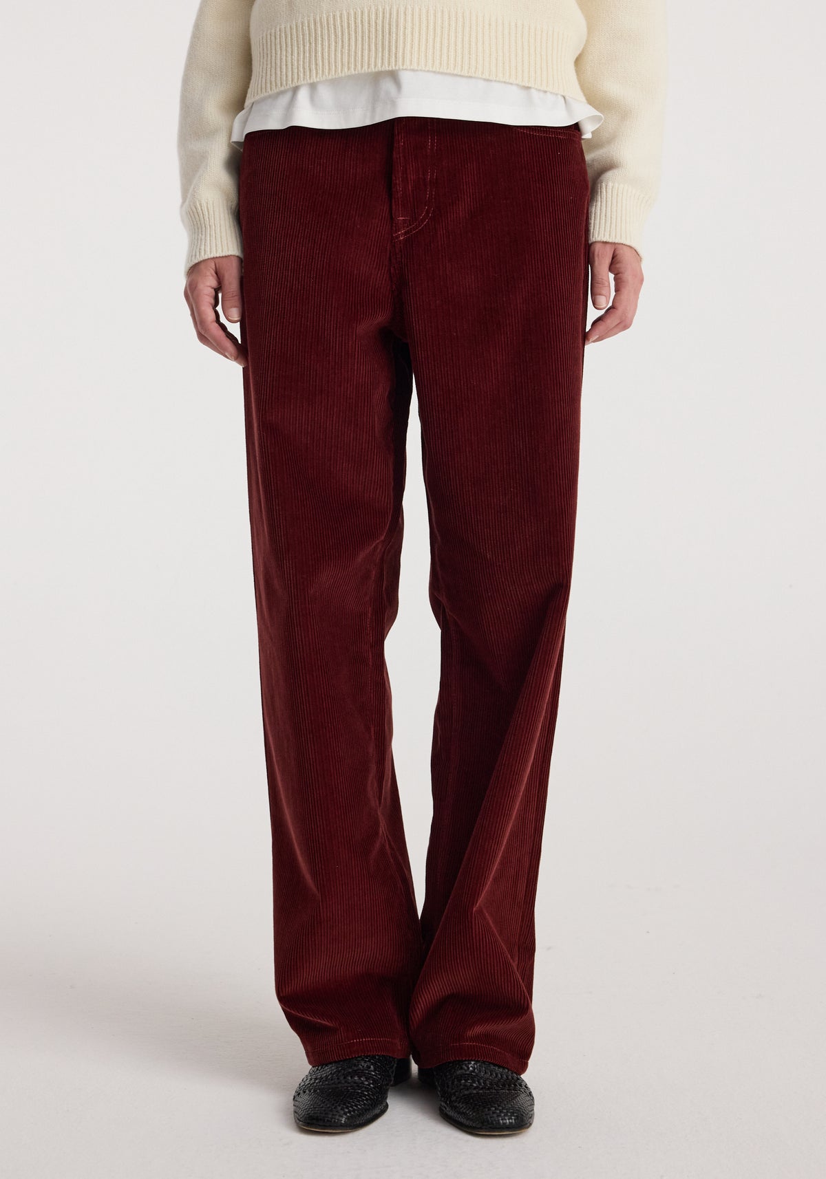 Front view of a person wearing Bruun - Signature baggy corduroy trousers | wine, paired with a cream sweater and black shoes against a plain background.