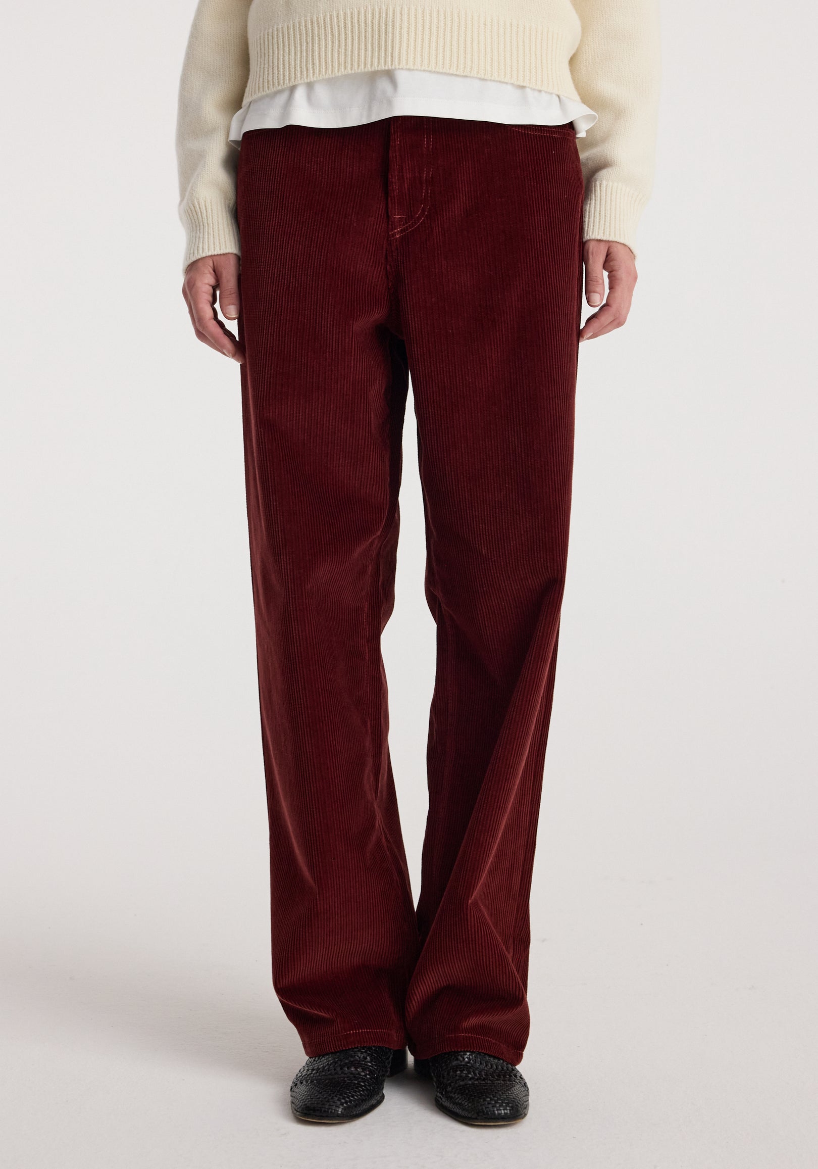 Front view of a person wearing Bruun - Signature baggy corduroy trousers | wine, paired with a cream sweater and black shoes against a plain background.