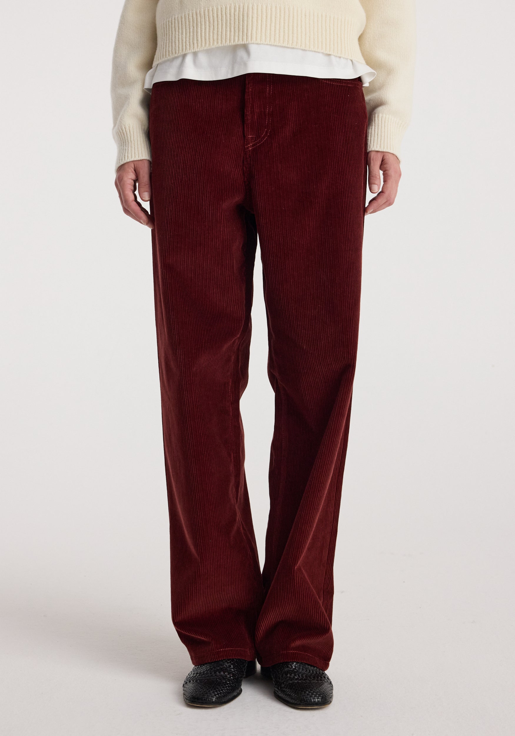 Front view of a person wearing Bruun - Signature baggy corduroy trousers | wine, paired with a cream sweater and black shoes against a plain background.