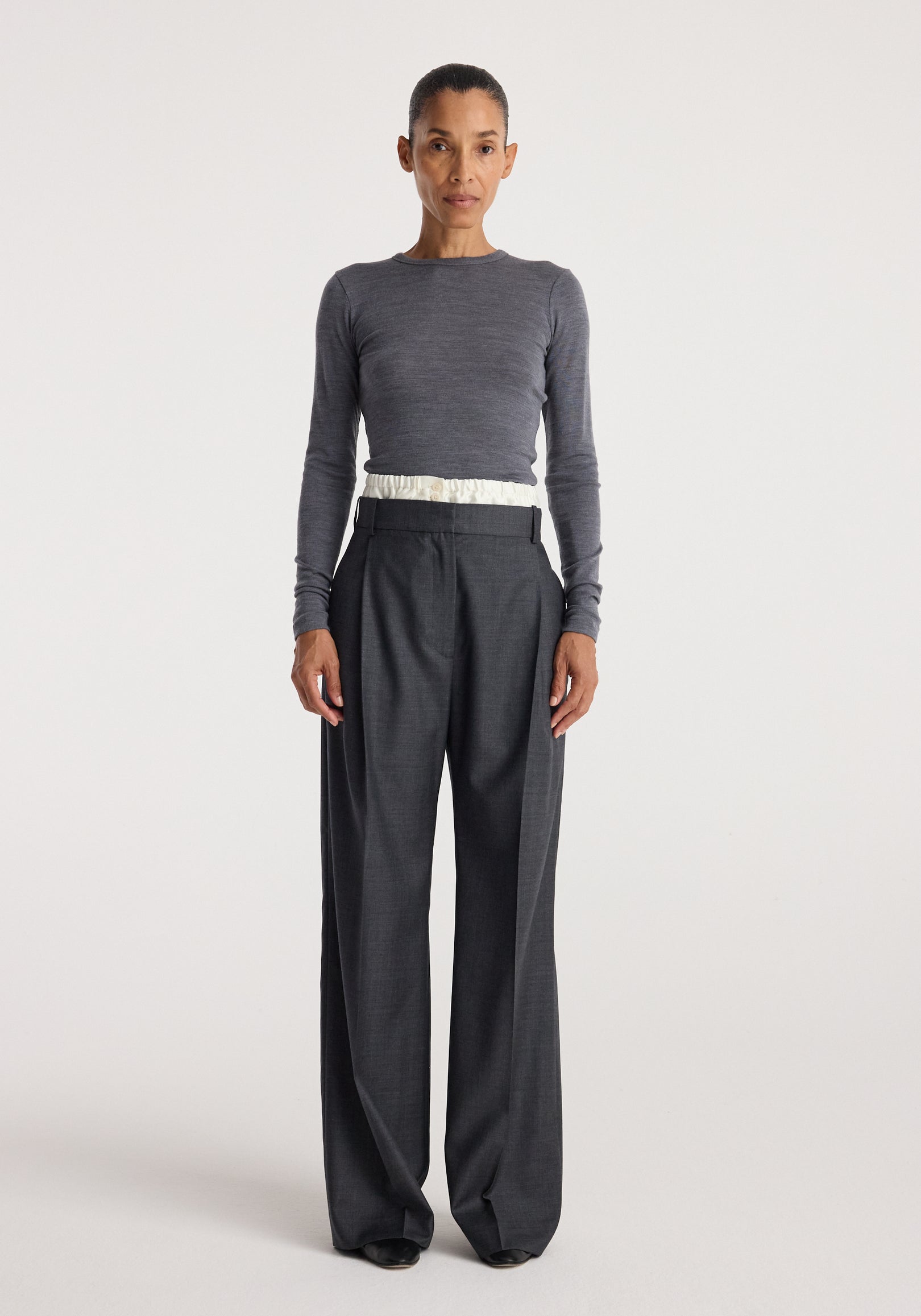 Woman wearing Boxer detailed trousers | dark grey melange with a high waist and wide-leg cut paired with a fitted long-sleeve grey top against a plain background.