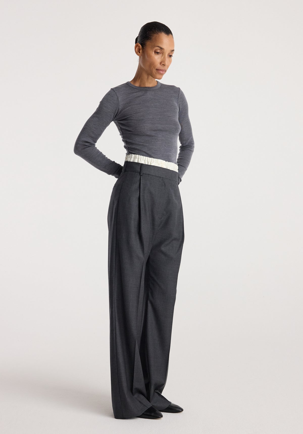 Woman wearing Boxer detailed trousers | dark grey melange styled with a fitted long-sleeve grey top, standing against a plain light background.
