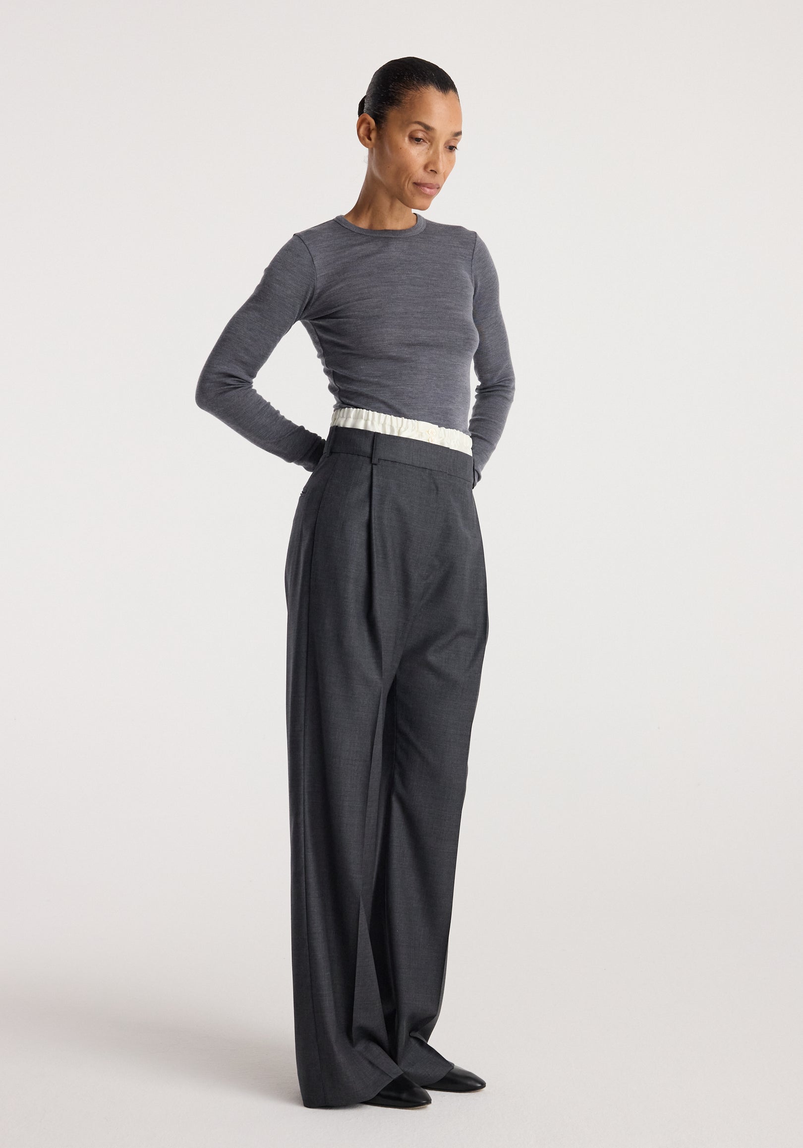 Woman wearing Boxer detailed trousers | dark grey melange styled with a fitted long-sleeve grey top, standing against a plain light background.