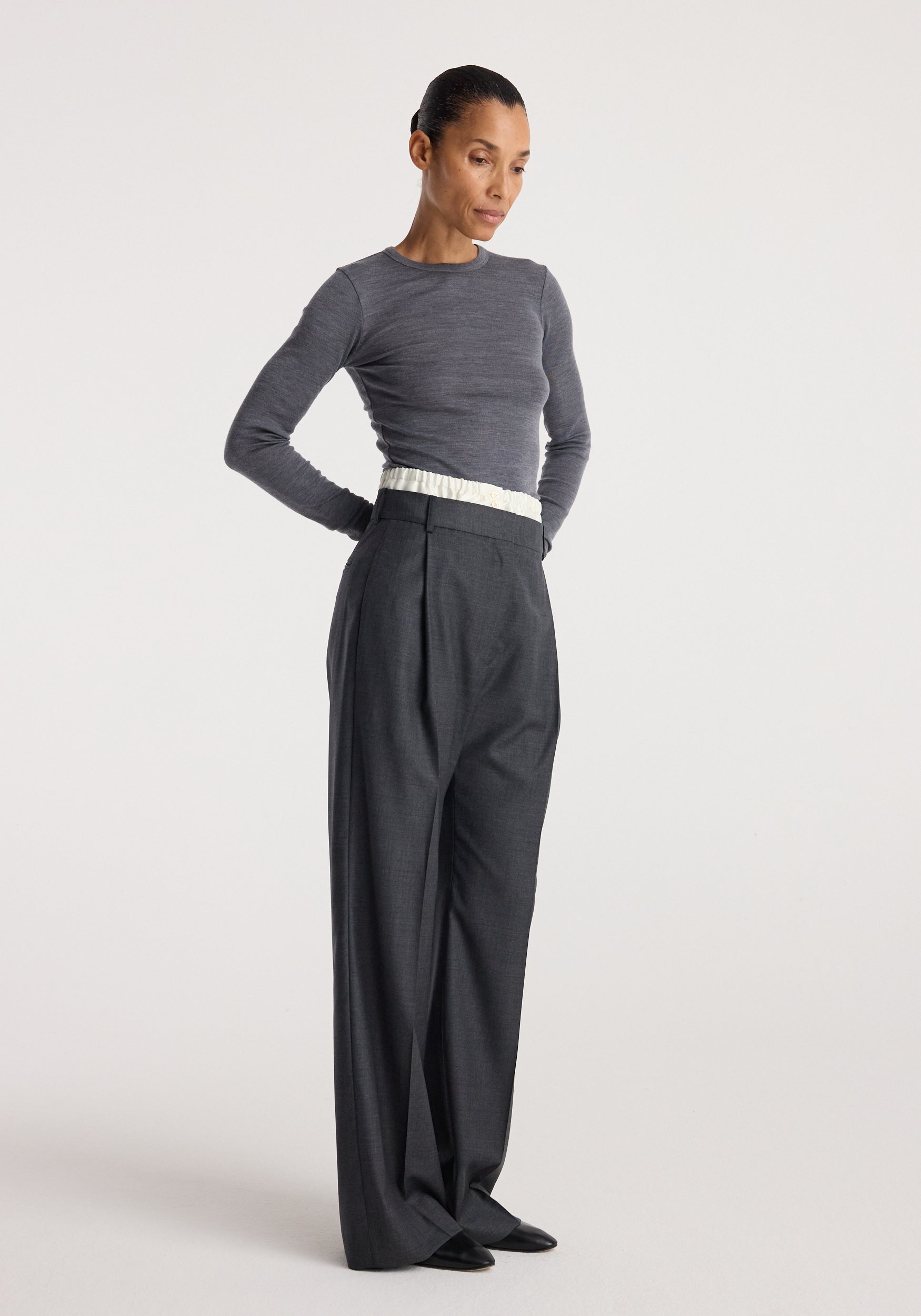 Woman wearing Boxer detailed trousers | dark grey melange styled with a fitted long-sleeve grey top, standing against a plain light background.