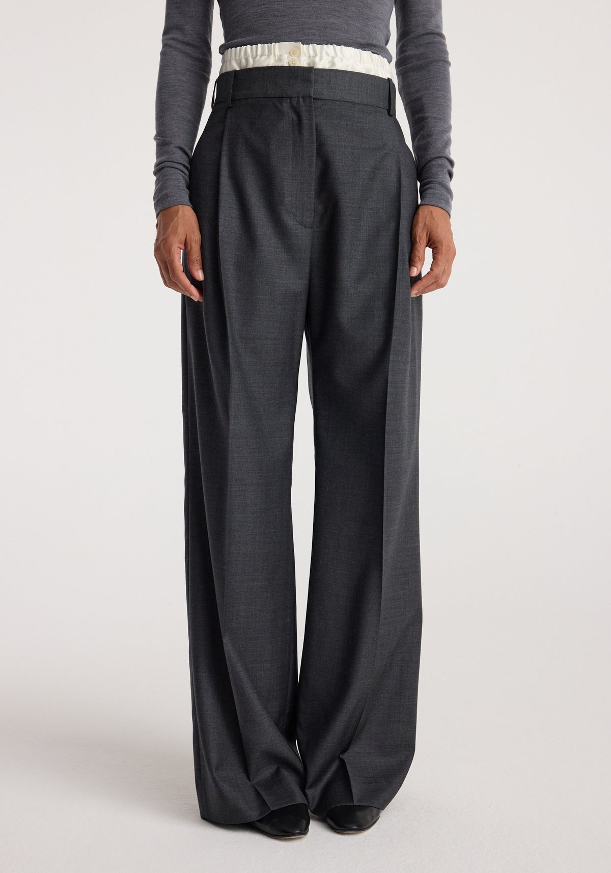 Front view of a person wearing Boxer detailed trousers | dark grey melange with a high waist, pleats, and wide legs paired with a long-sleeve fitted top.