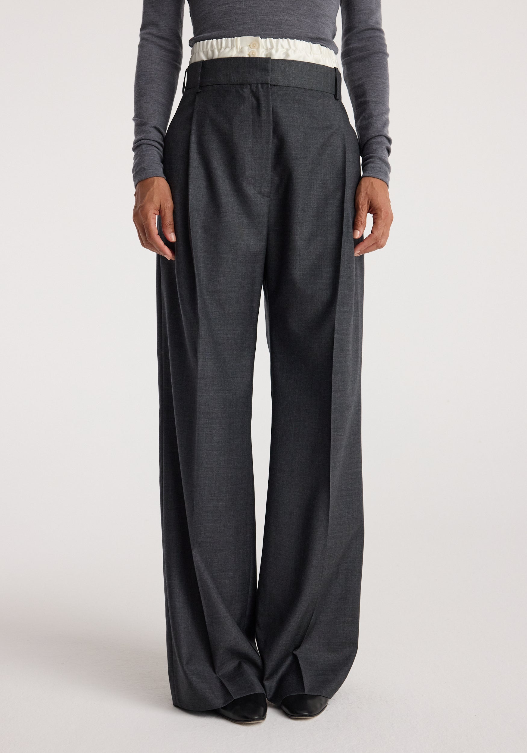 Front view of a person wearing Boxer detailed trousers | dark grey melange with a high waist, pleats, and wide legs paired with a long-sleeve fitted top.