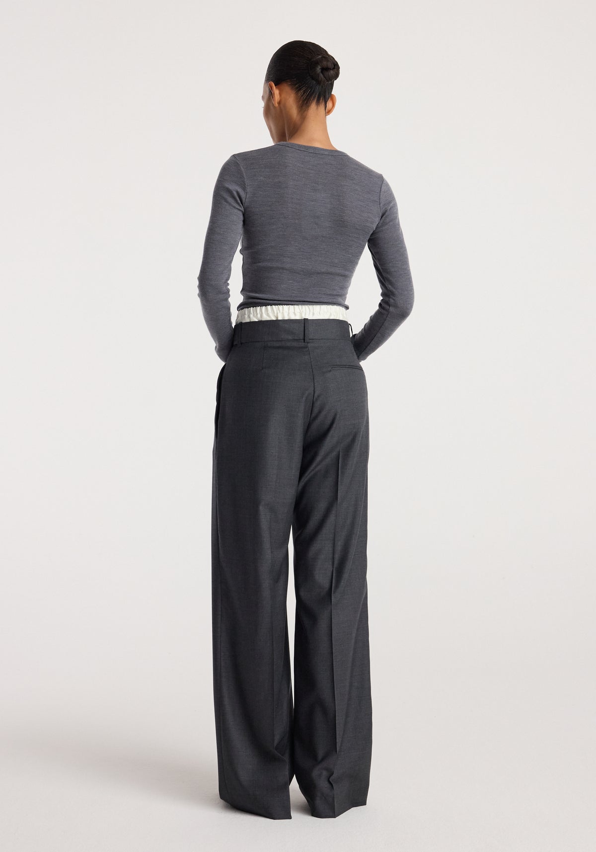 Woman wearing dark grey melange long sleeve top and loose fitting Boxer detailed trousers | dark grey melange, viewed from the back against a plain background