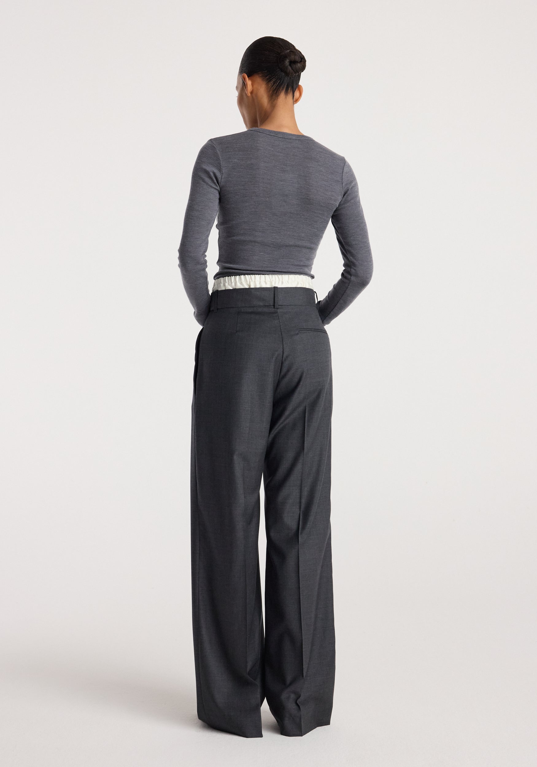 Woman wearing dark grey melange long sleeve top and loose fitting Boxer detailed trousers | dark grey melange, viewed from the back against a plain background