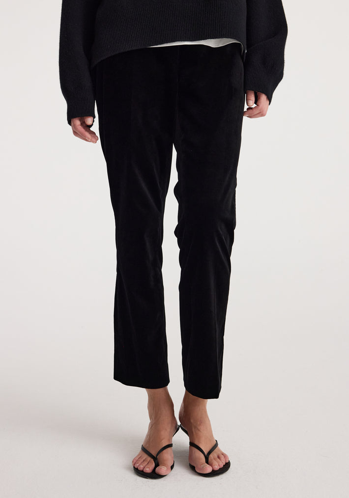 Front view of a person wearing cigarette leg velvet tailored trousers | black, styled with a black top and black open-toe sandals.