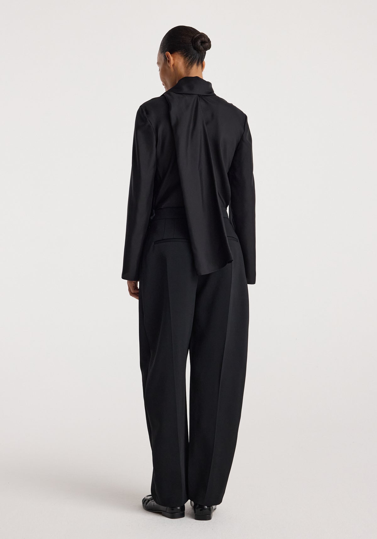 Back view of a model wearing black sculptural tailored trousers with a high waist and relaxed tapered legs, Puck - Sculptural tailored trousers | black