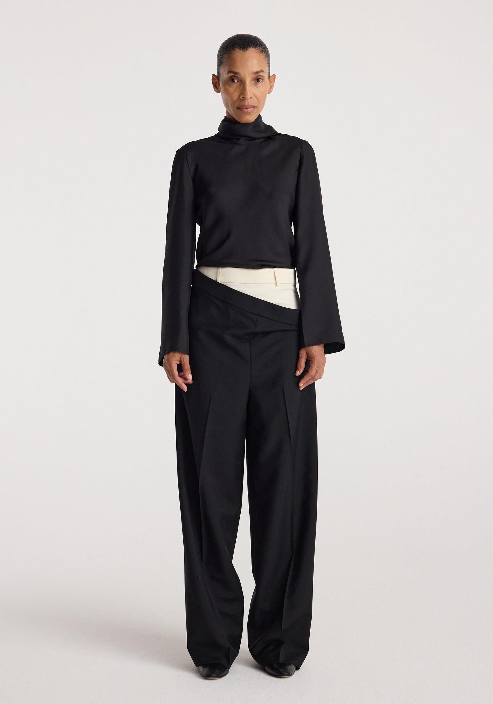 Woman wearing black long-sleeve high-neck top paired with Double waistband trousers | black featuring a unique overlapping waistband design and wide-leg fit.