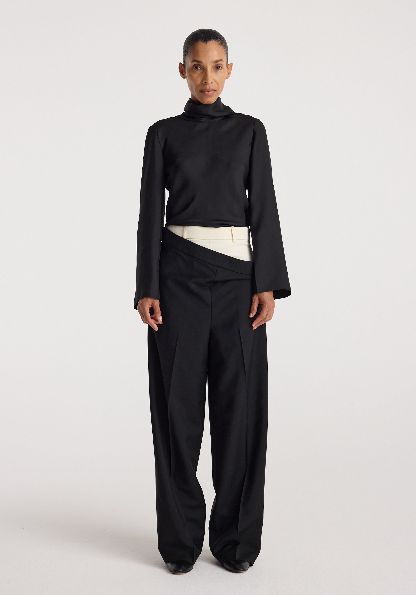Woman wearing black long-sleeve high-neck top paired with Double waistband trousers | black featuring a unique overlapping waistband design and wide-leg fit.