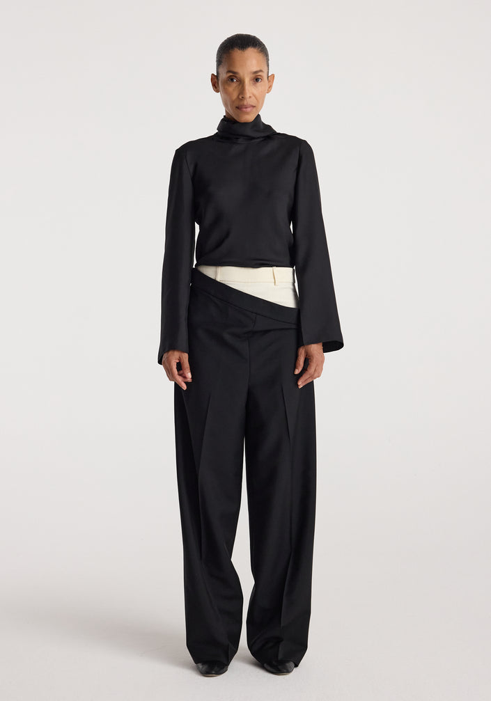 Woman wearing black long-sleeve high-neck top paired with Double waistband trousers | black featuring a unique overlapping waistband design and wide-leg fit.