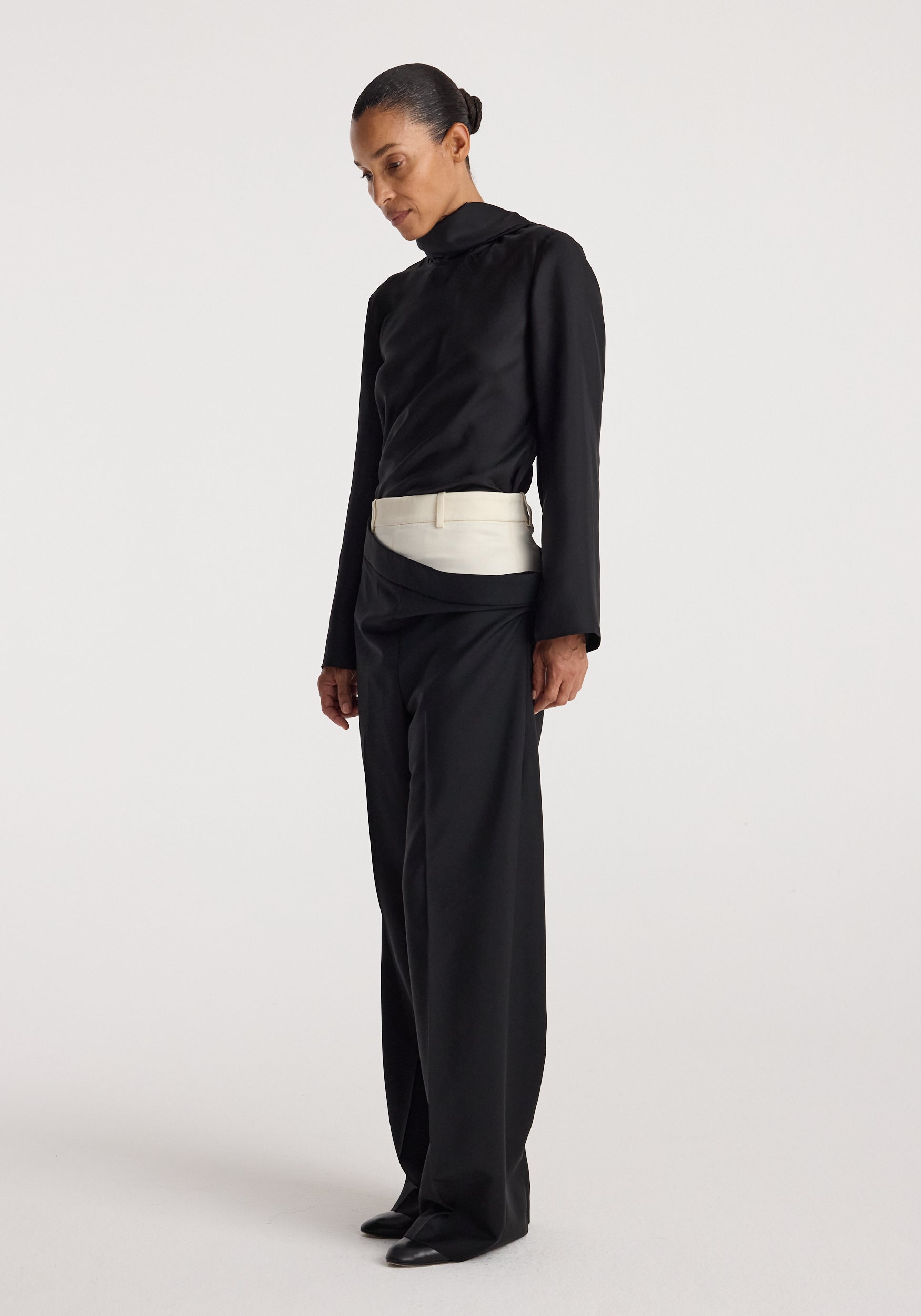 Model wearing Double waistband trousers | black with a contrasting light-colored double waistband detail, paired with a black long-sleeve top and black shoes, standing against a plain background.