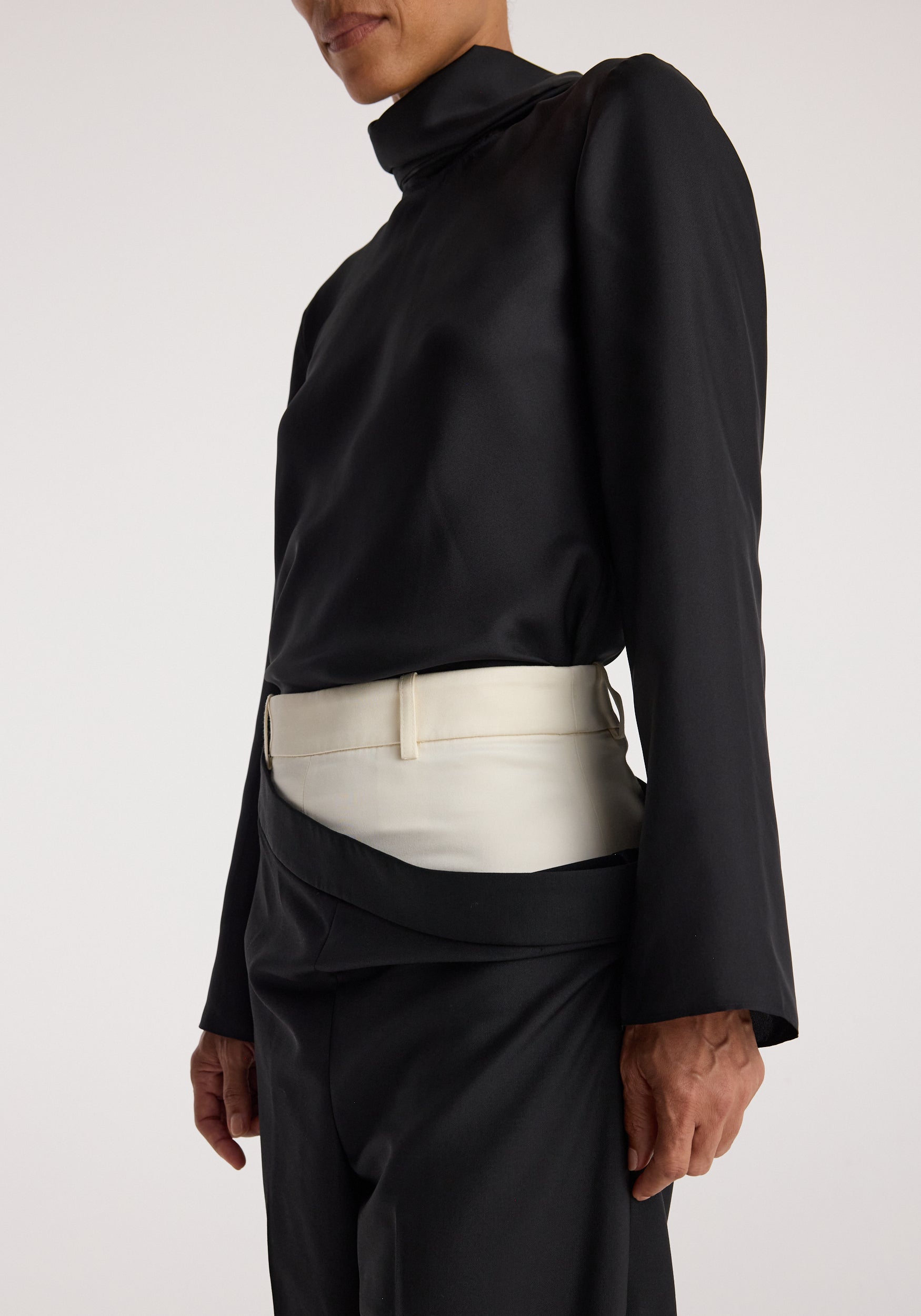 Close-up of a person wearing Double waistband trousers | black featuring an overlapping double waistband design with one black and one white layer, paired with a black long-sleeve top.