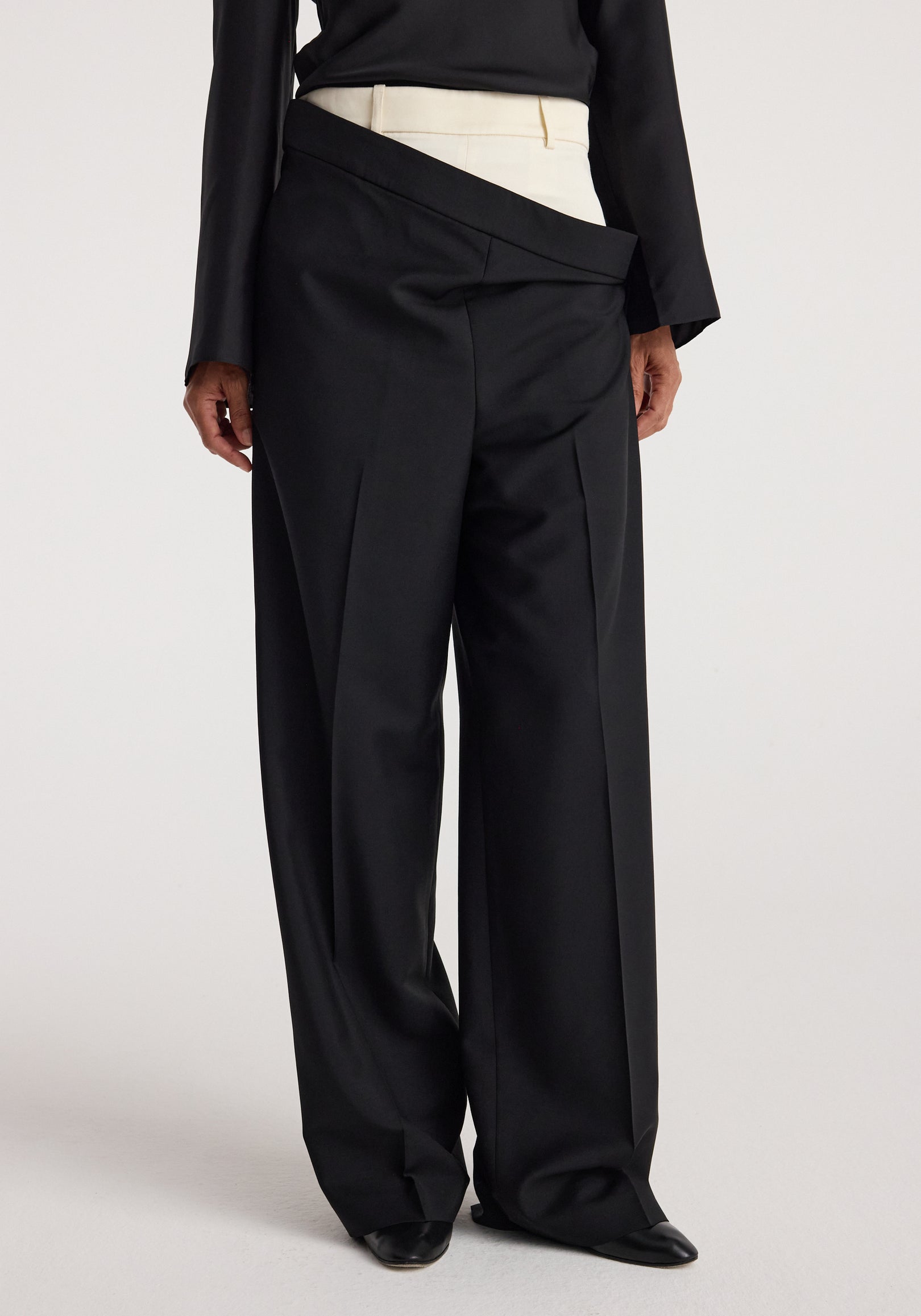 A model wearing black Double waistband trousers | black with a unique overlapping waistband design paired with a black long-sleeve top and white inner waistband detail.
