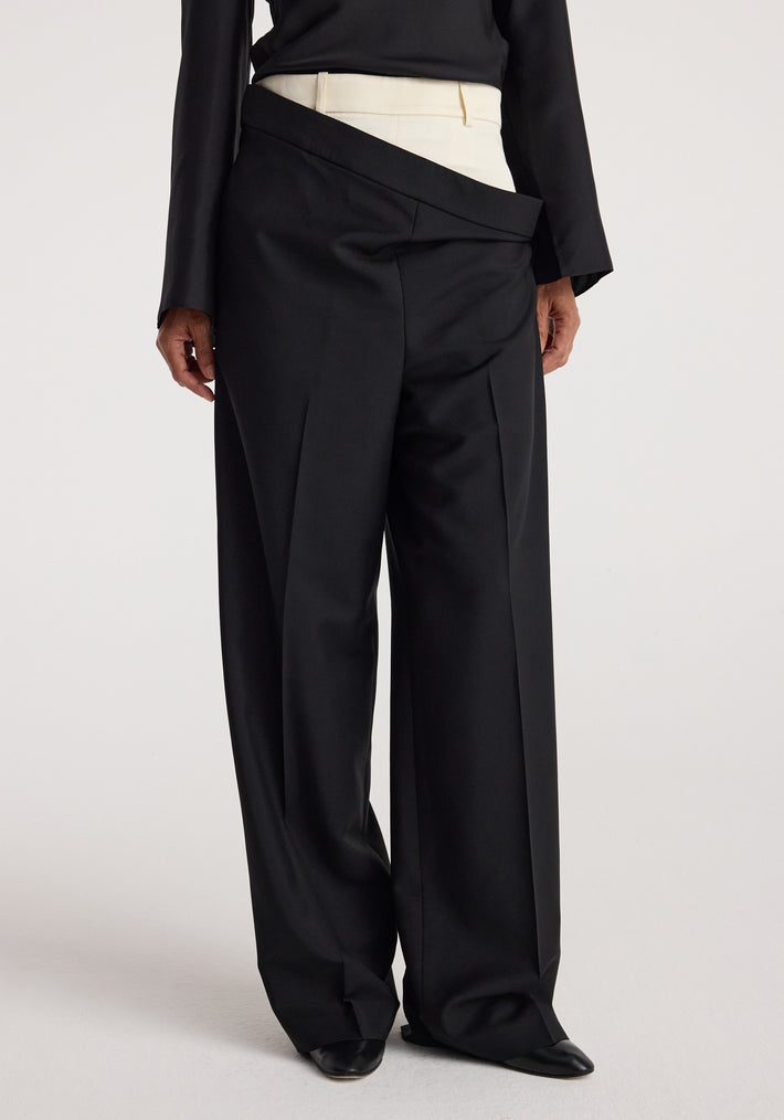A model wearing black Double waistband trousers | black with a unique overlapping waistband design paired with a black long-sleeve top and white inner waistband detail.