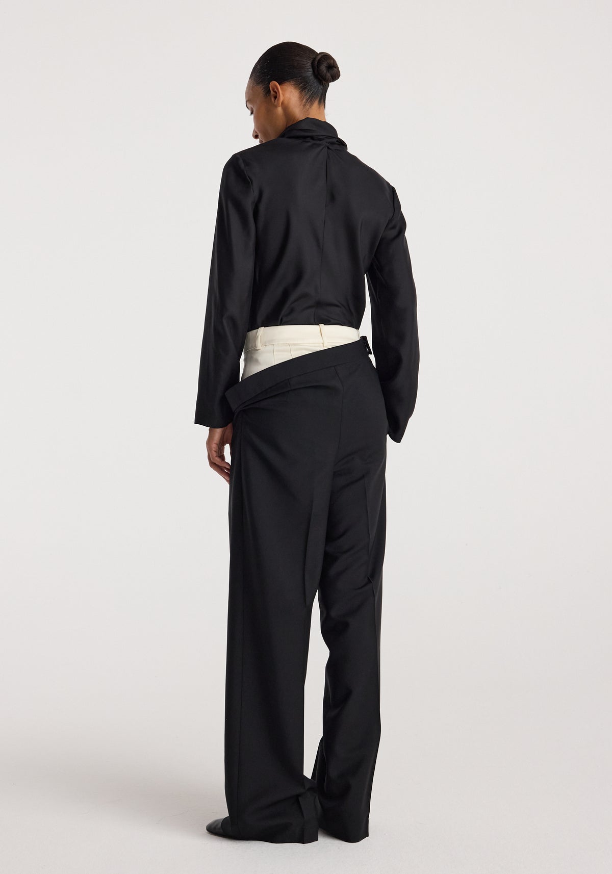 Back view of a person wearing double waistband trousers | black paired with a black long-sleeve top, showcasing the unique layered waistband design.