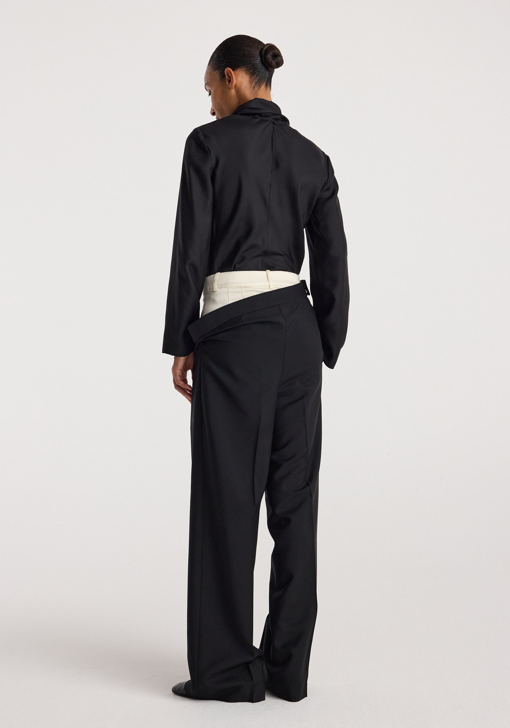 Back view of a person wearing double waistband trousers | black paired with a black long-sleeve top, showcasing the unique layered waistband design.