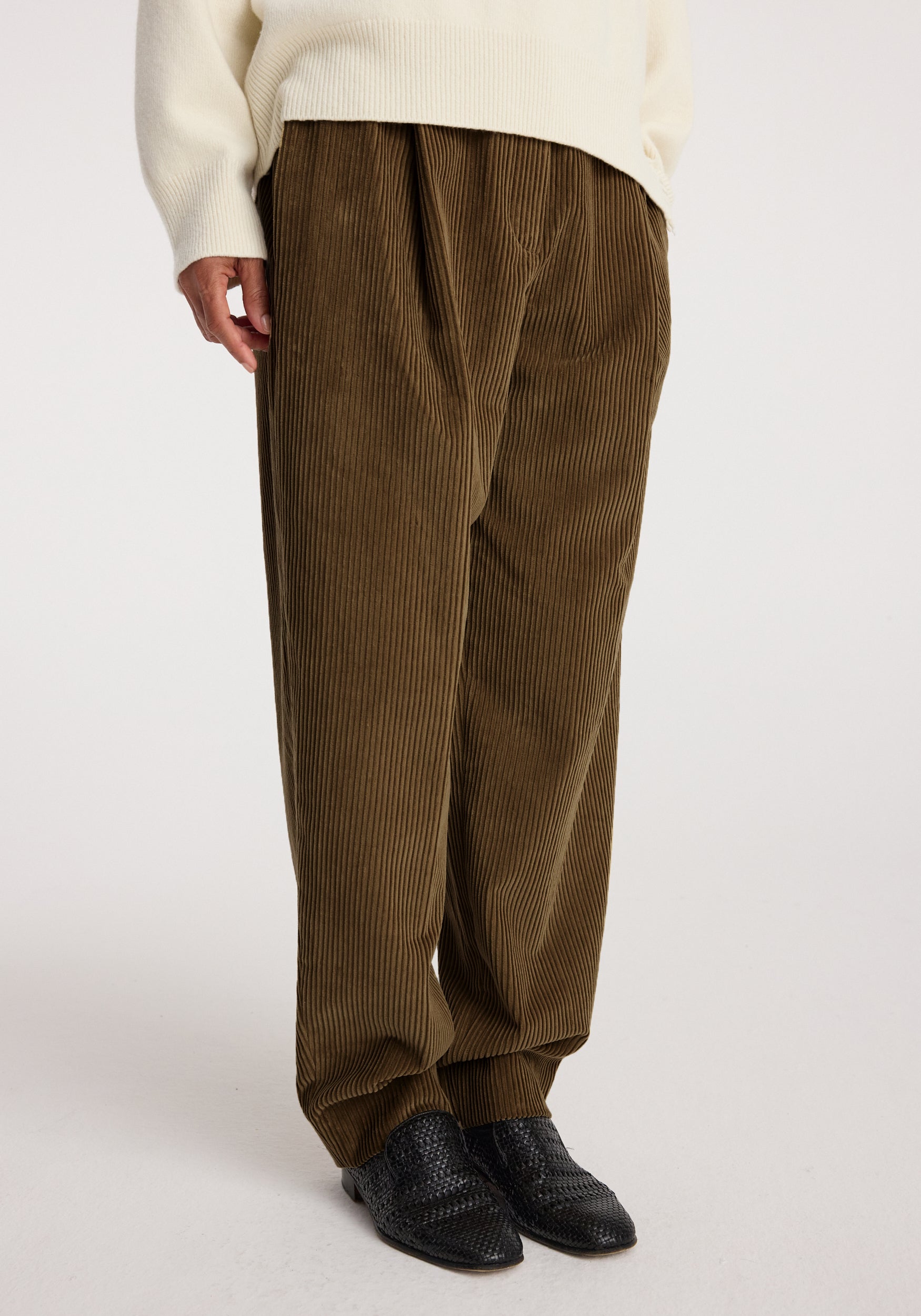 Close-up of a person wearing caramel colored Daria - Single pleat straight leg corduroy trousers paired with a cream sweater and black textured shoes.