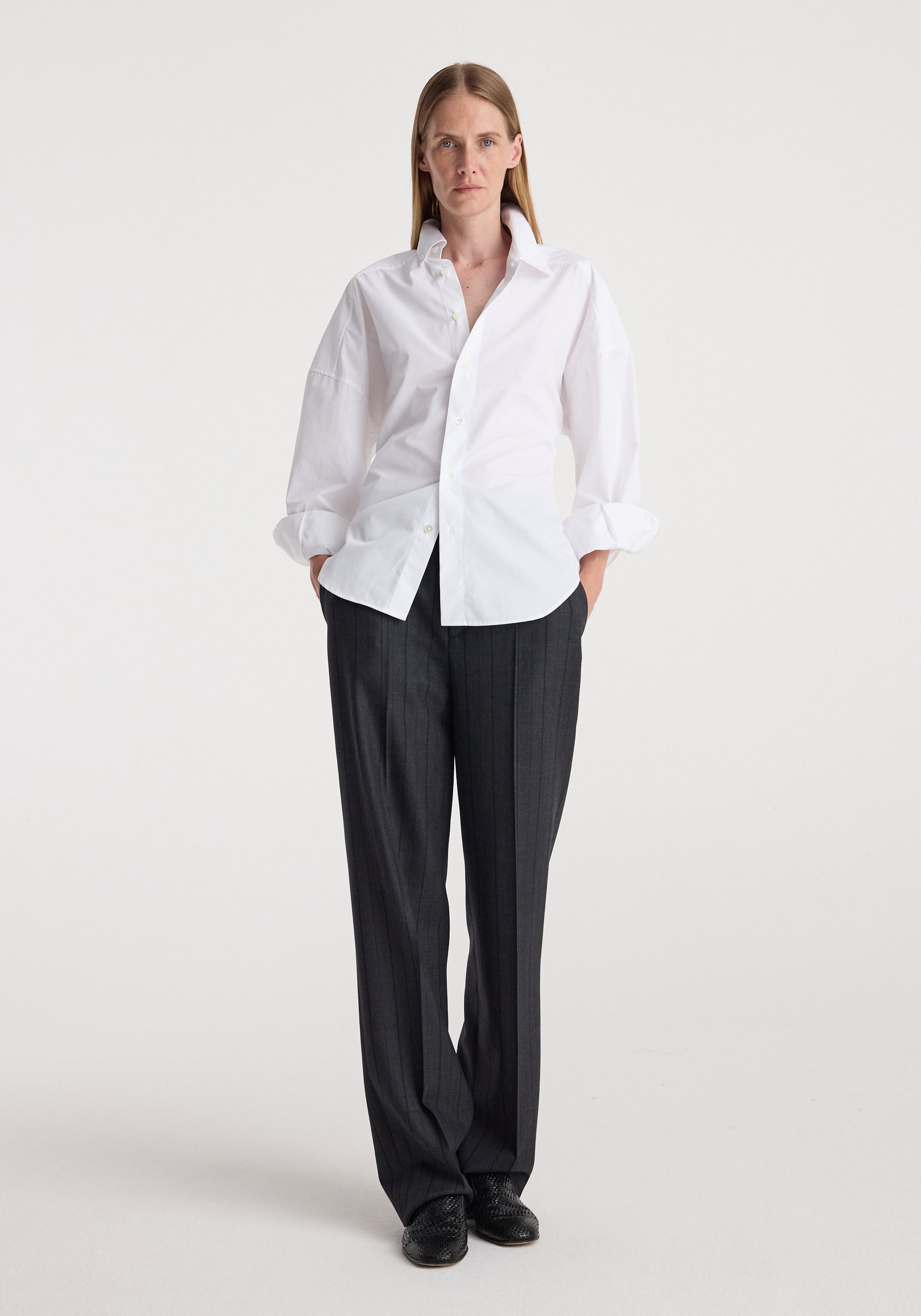 Woman wearing Kee - Straight leg tailored trousers | charcoal stripe paired with a crisp white shirt and black shoes, standing against a plain white background.