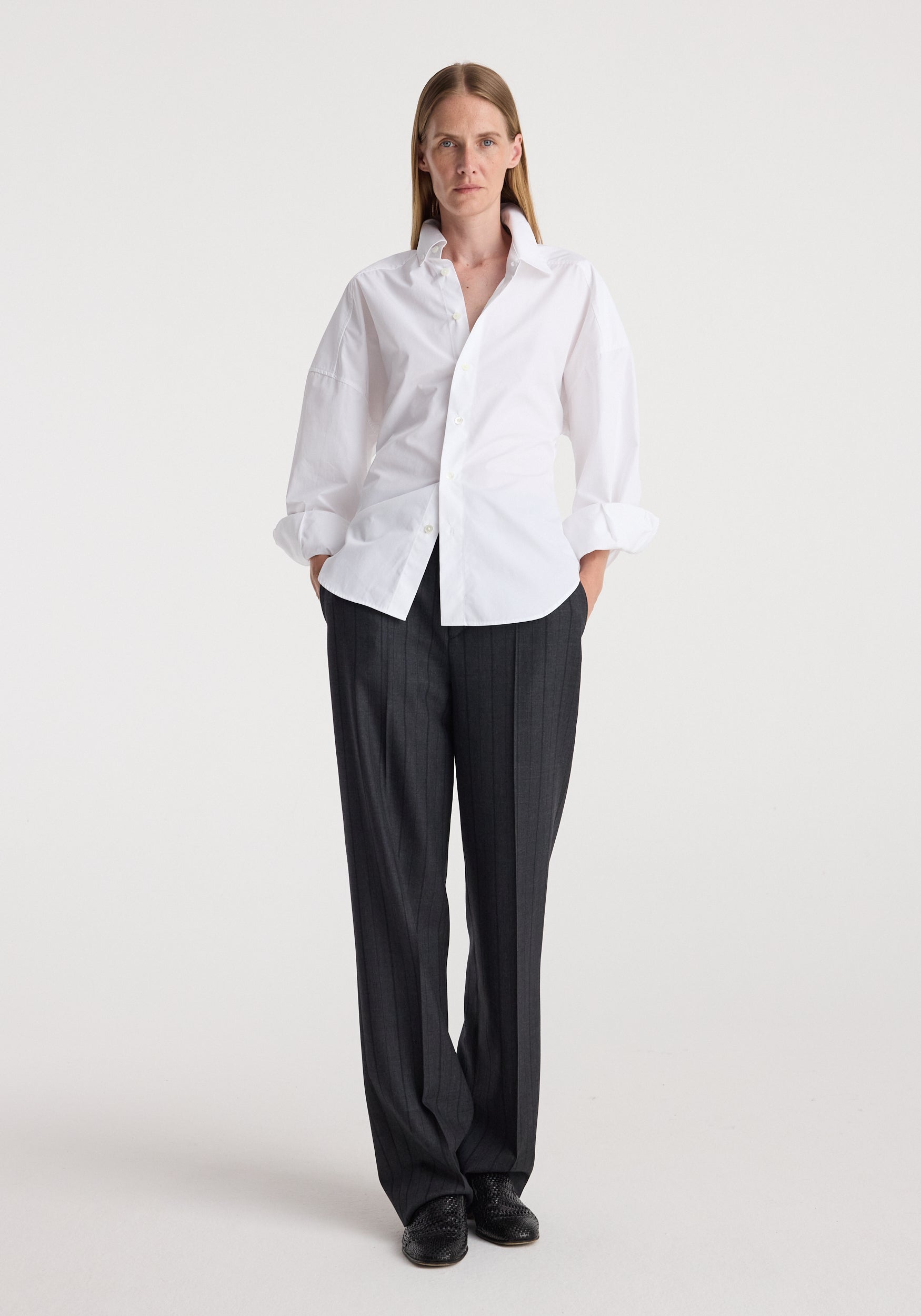 Woman wearing Kee - Straight leg tailored trousers | charcoal stripe paired with a crisp white shirt and black shoes, standing against a plain white background.