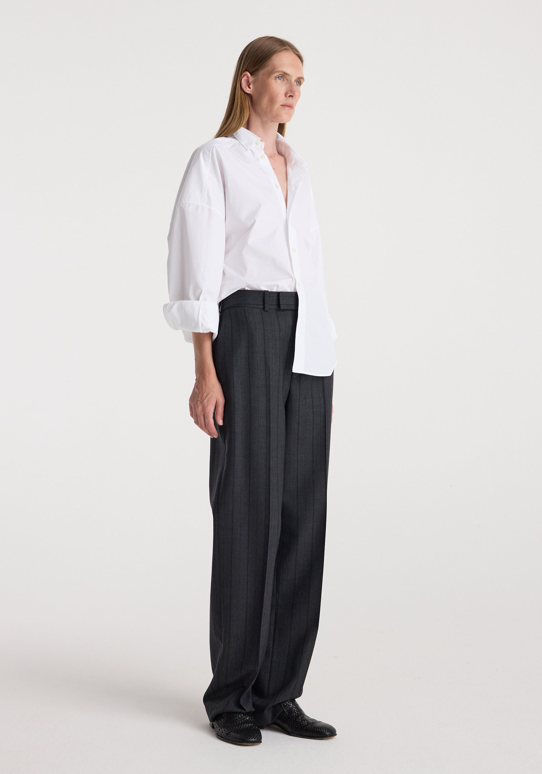 Woman wearing Kee - Straight leg tailored trousers | charcoal stripe paired with a white button-up shirt and black shoes, standing against a plain background.