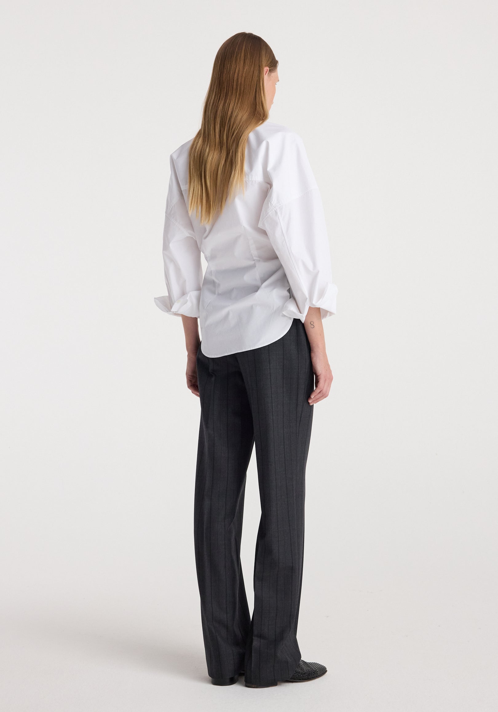 Woman wearing Kee - Straight leg tailored trousers | charcoal stripe, styled with a white long-sleeve shirt, shown from the back against a plain background.