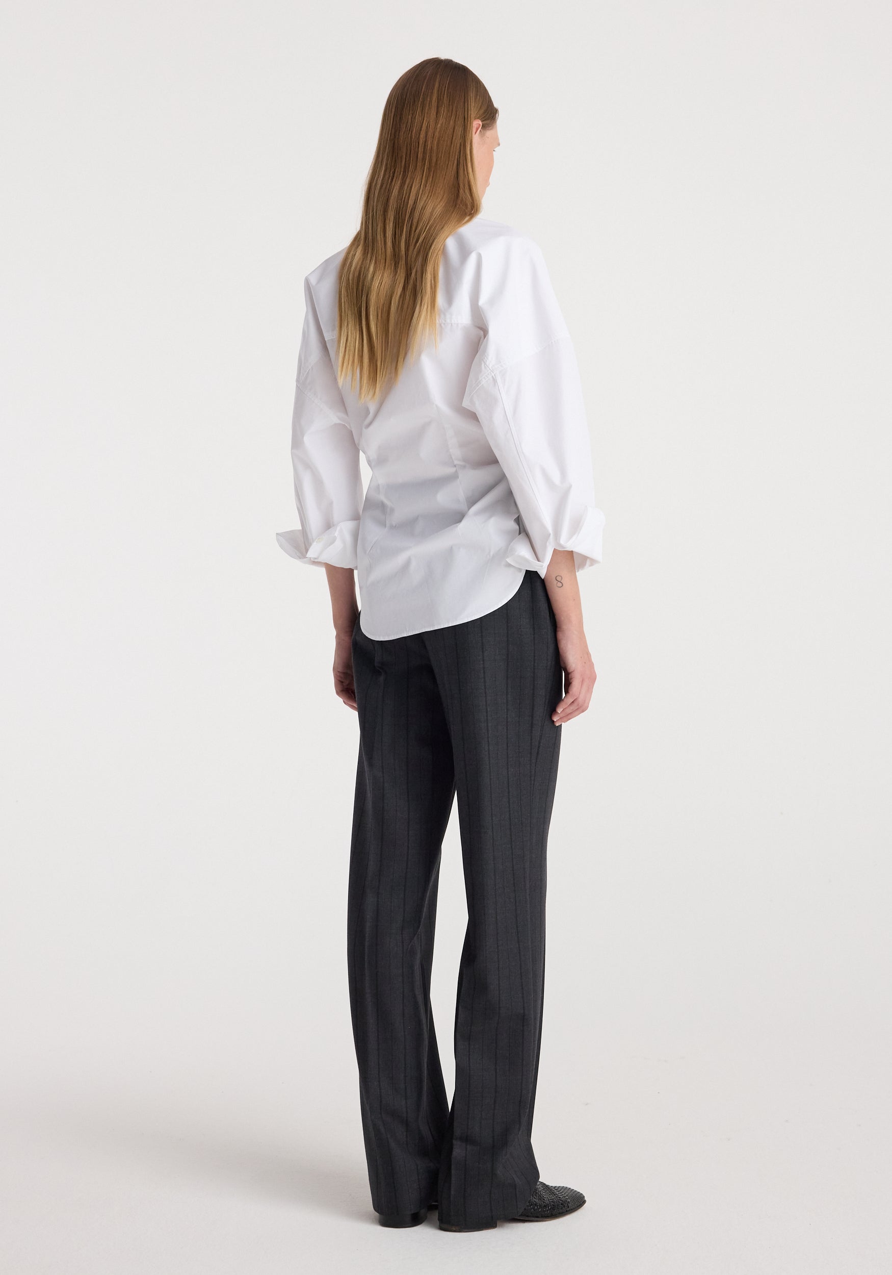 Woman wearing Kee - Straight leg tailored trousers | charcoal stripe, styled with a white long-sleeve shirt, shown from the back against a plain background.