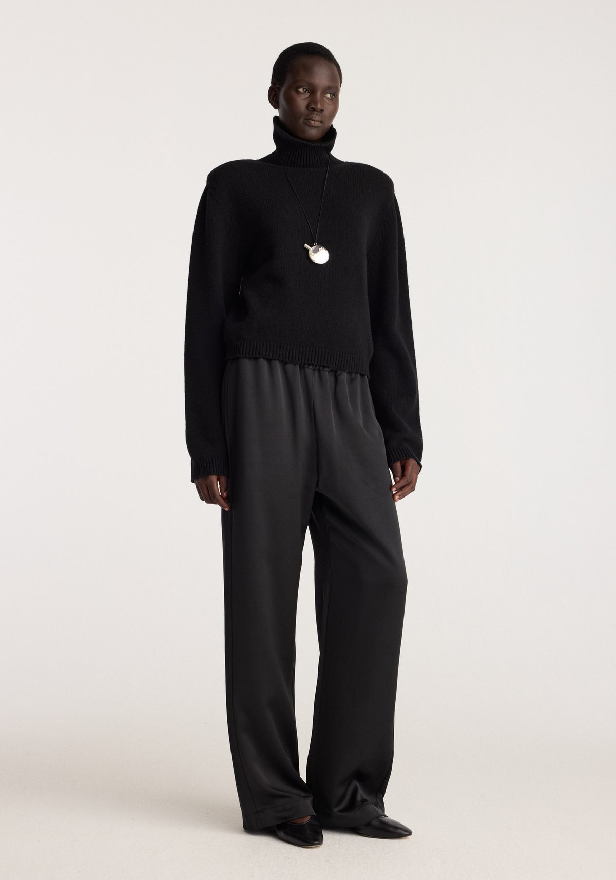 Perfume bottle silver necklace | silver worn by a model over a black turtleneck sweater with a small silver perfume bottle pendant visible at the chest